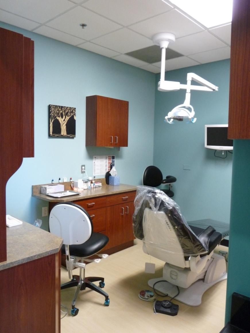 Dental office room with teal walls, wood cabinets, dental chair, and light.