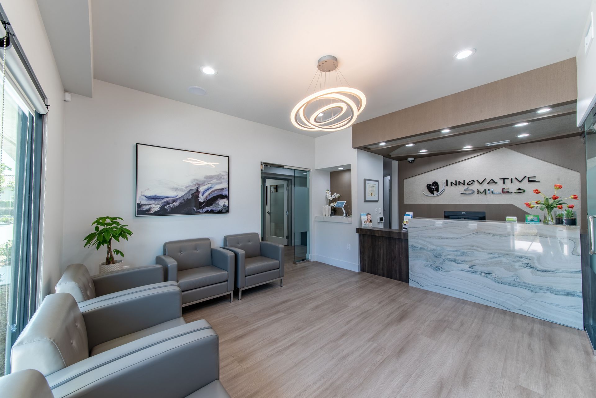 Modern waiting room with gray chairs, a marble reception desk, and a decorative light fixture.
