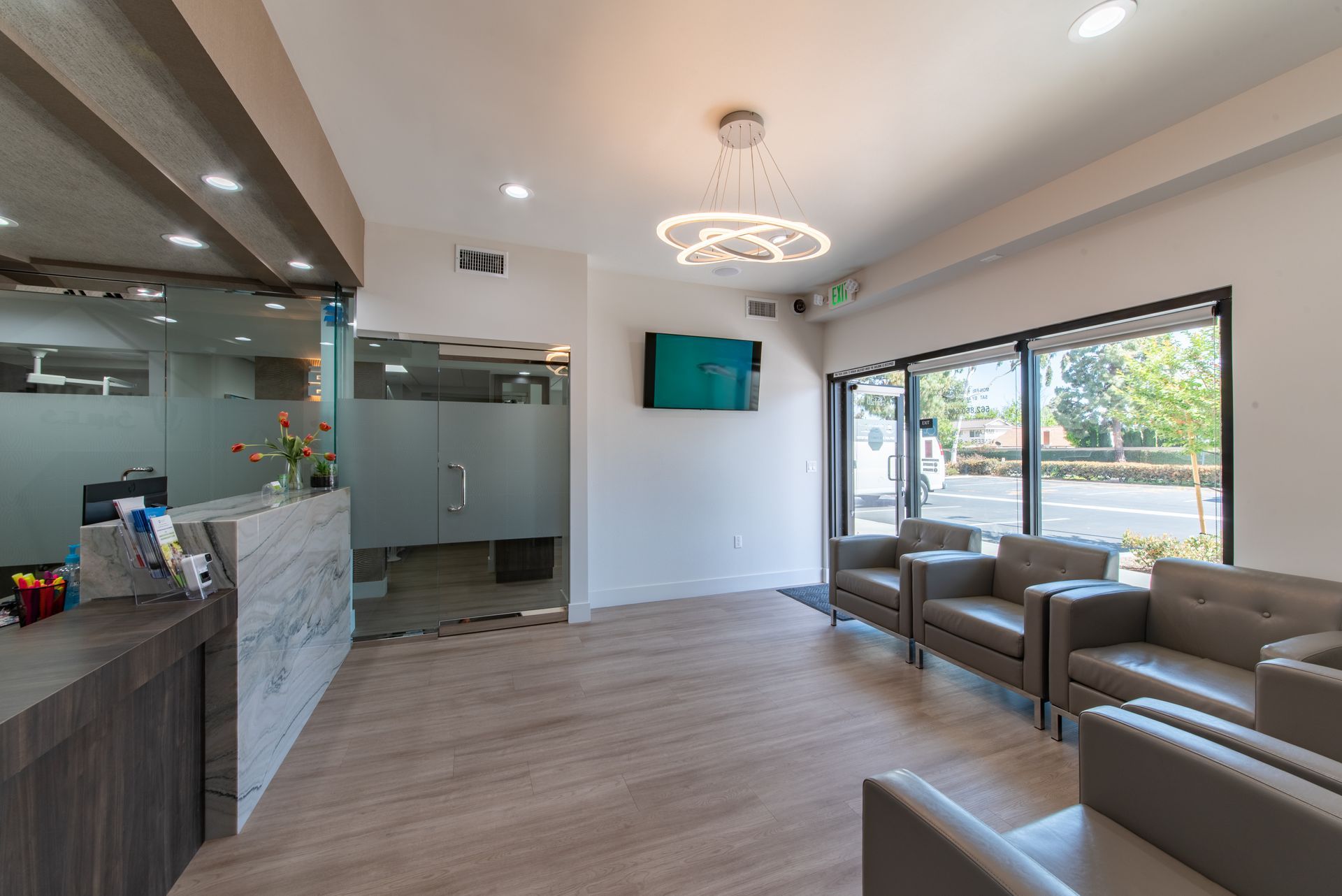 Modern dentist office waiting area with seating, reception desk, and frosted glass doors.