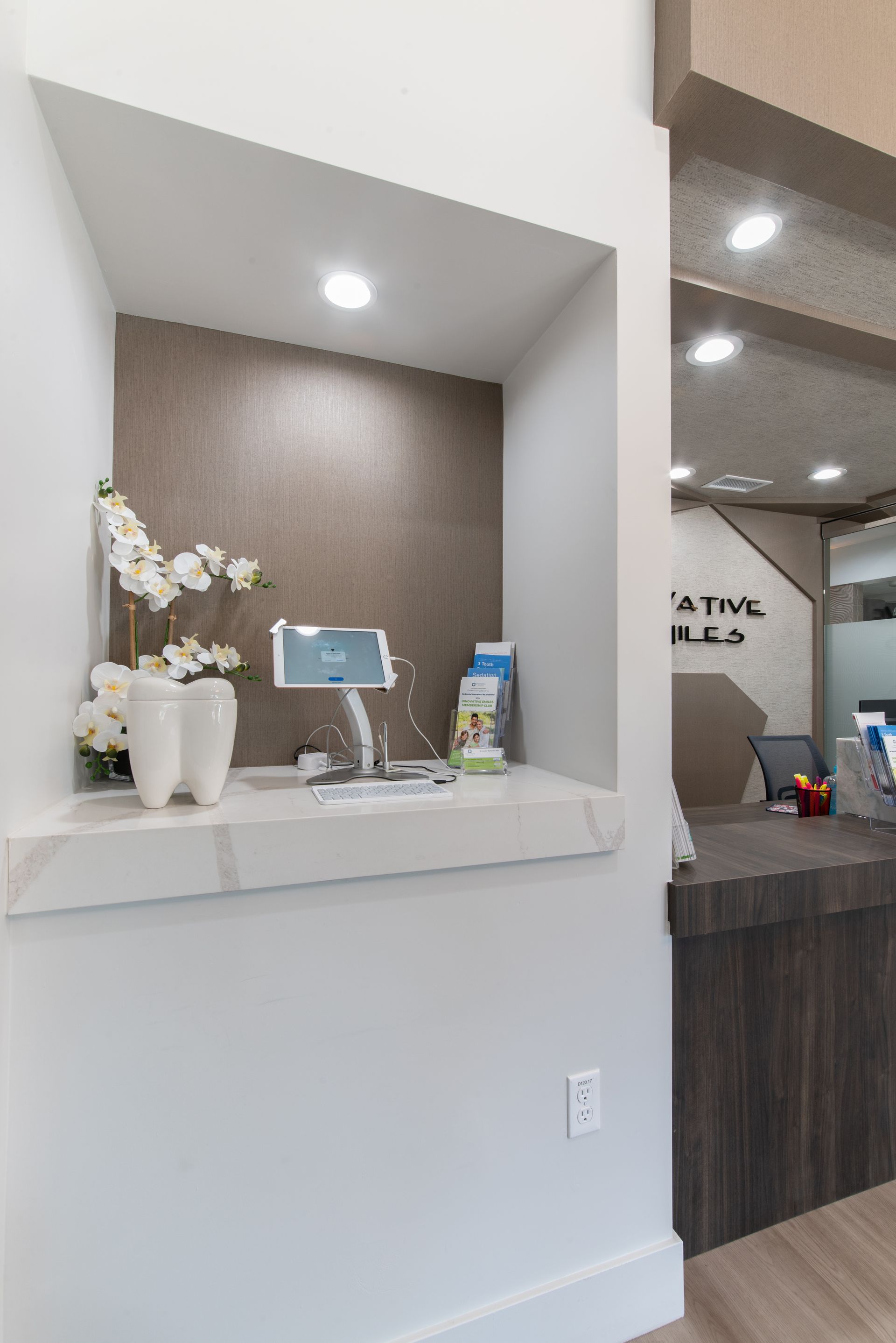 Reception area with built-in display niche; white countertop, dental decor, and a computer; modern design.