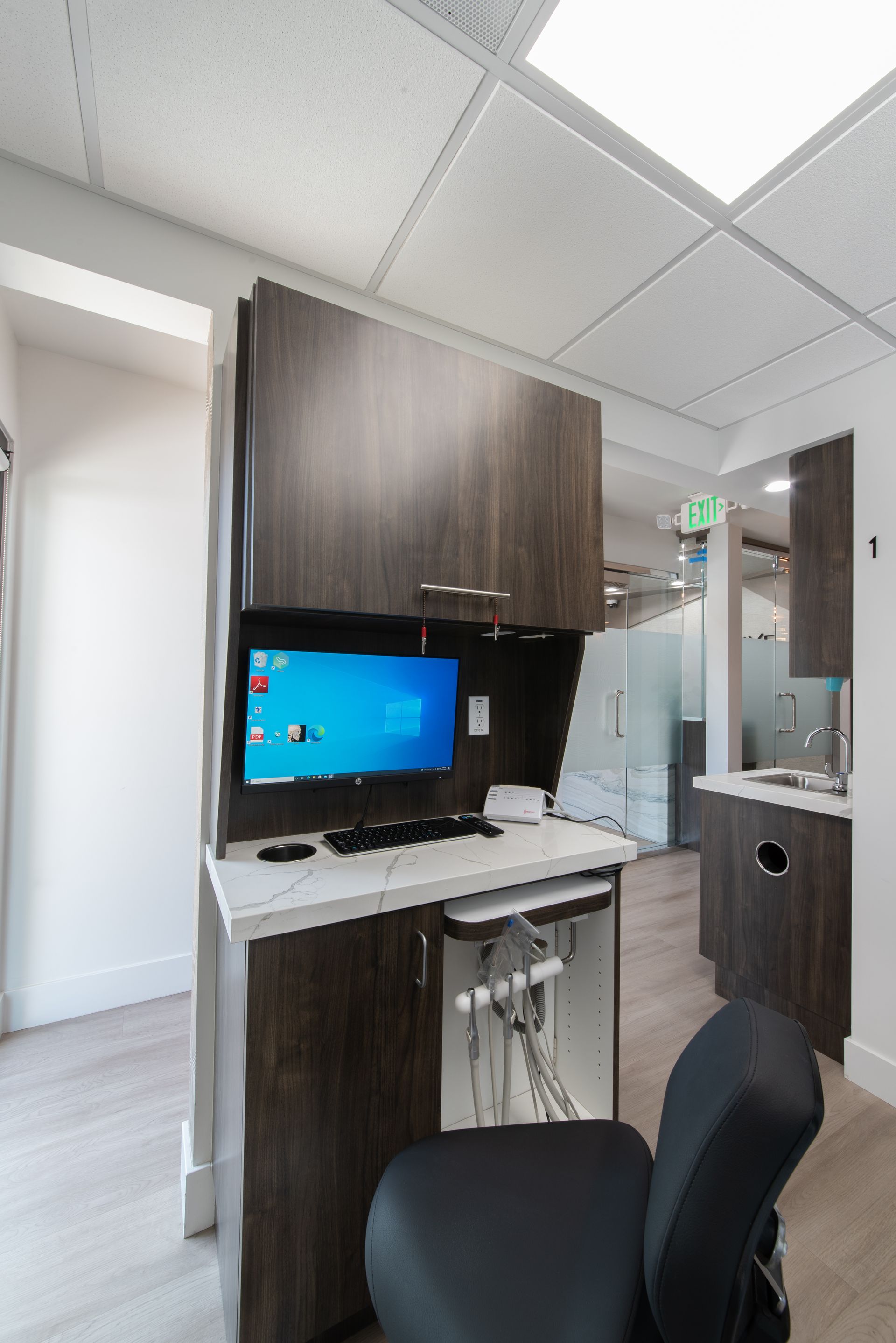 A dental office computer station. Dark wood cabinets with a monitor, keyboard, and dental tools.