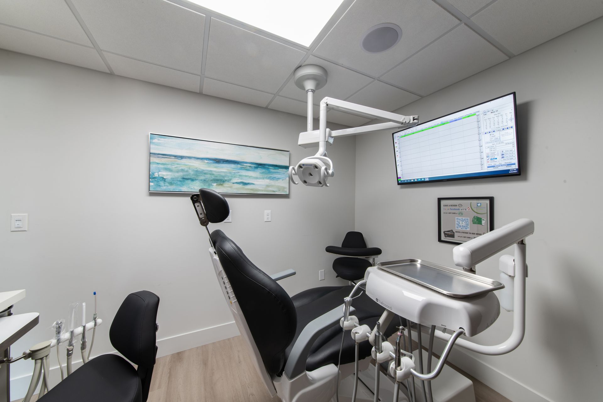 Dental office room with chair, equipment, mounted screen, and artwork.