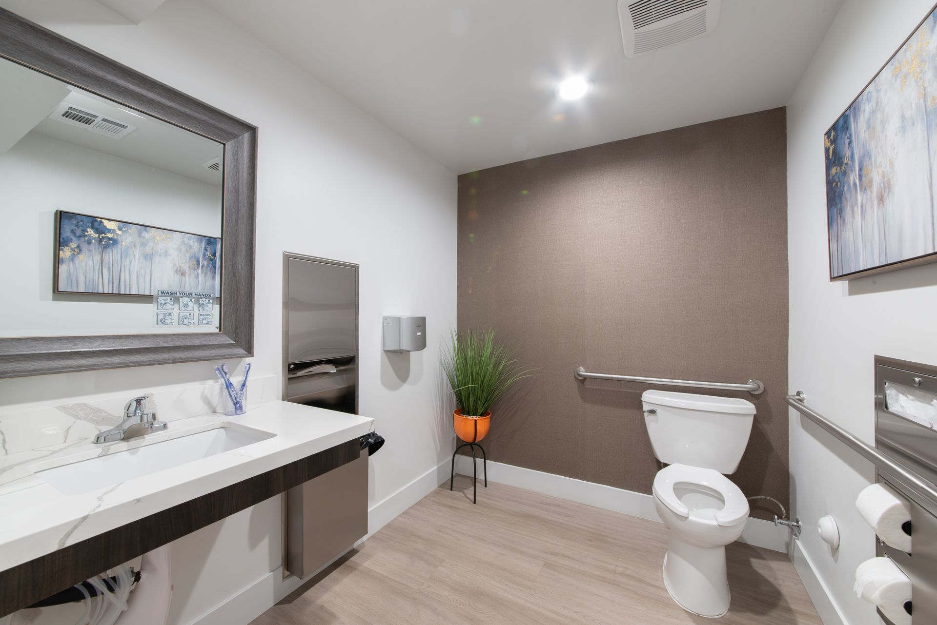 Accessible bathroom with sink, toilet, handrails, and artwork.