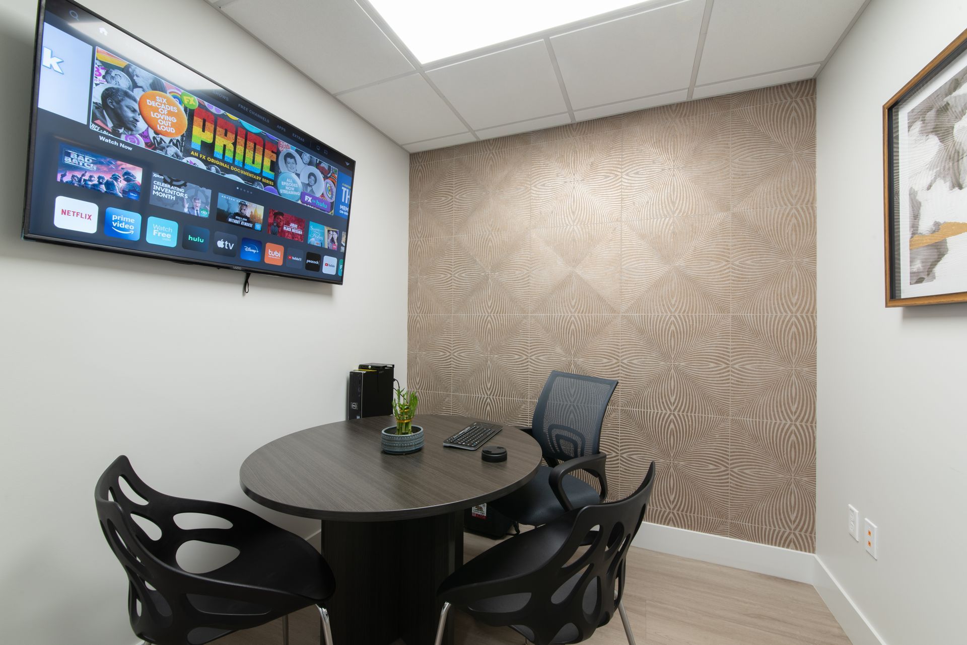 Meeting room with round table, chairs, TV, patterned wall, and framed art.