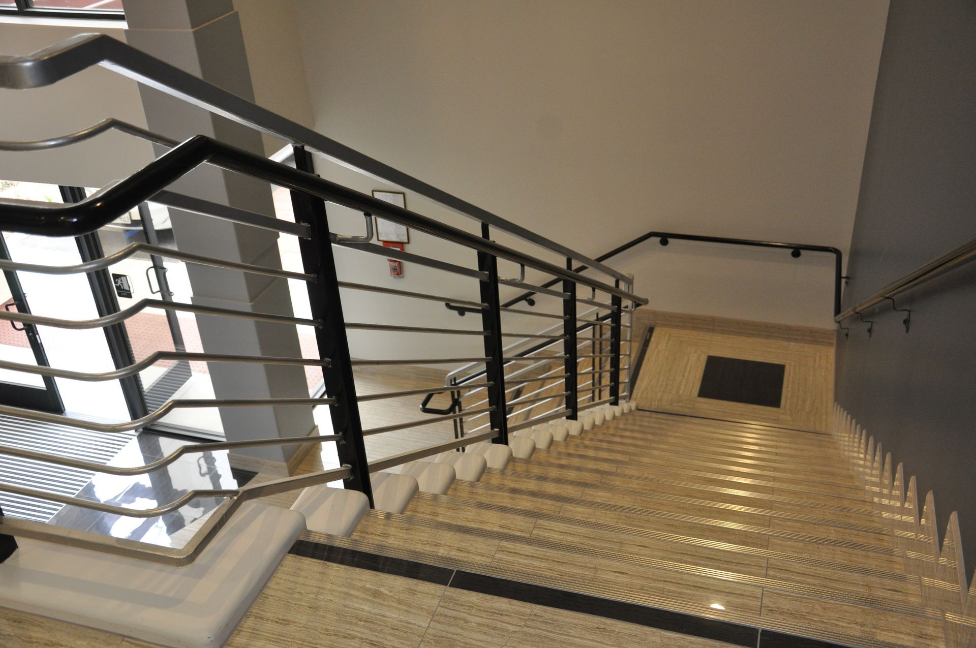 Staircase with metal railings, beige steps, and white walls, viewed from above.