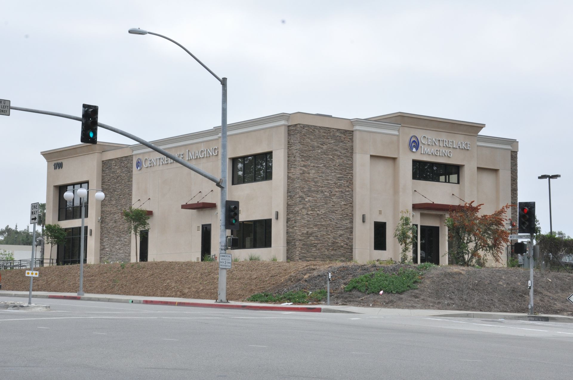 Two-story beige building with stone accents, traffic lights, and street.