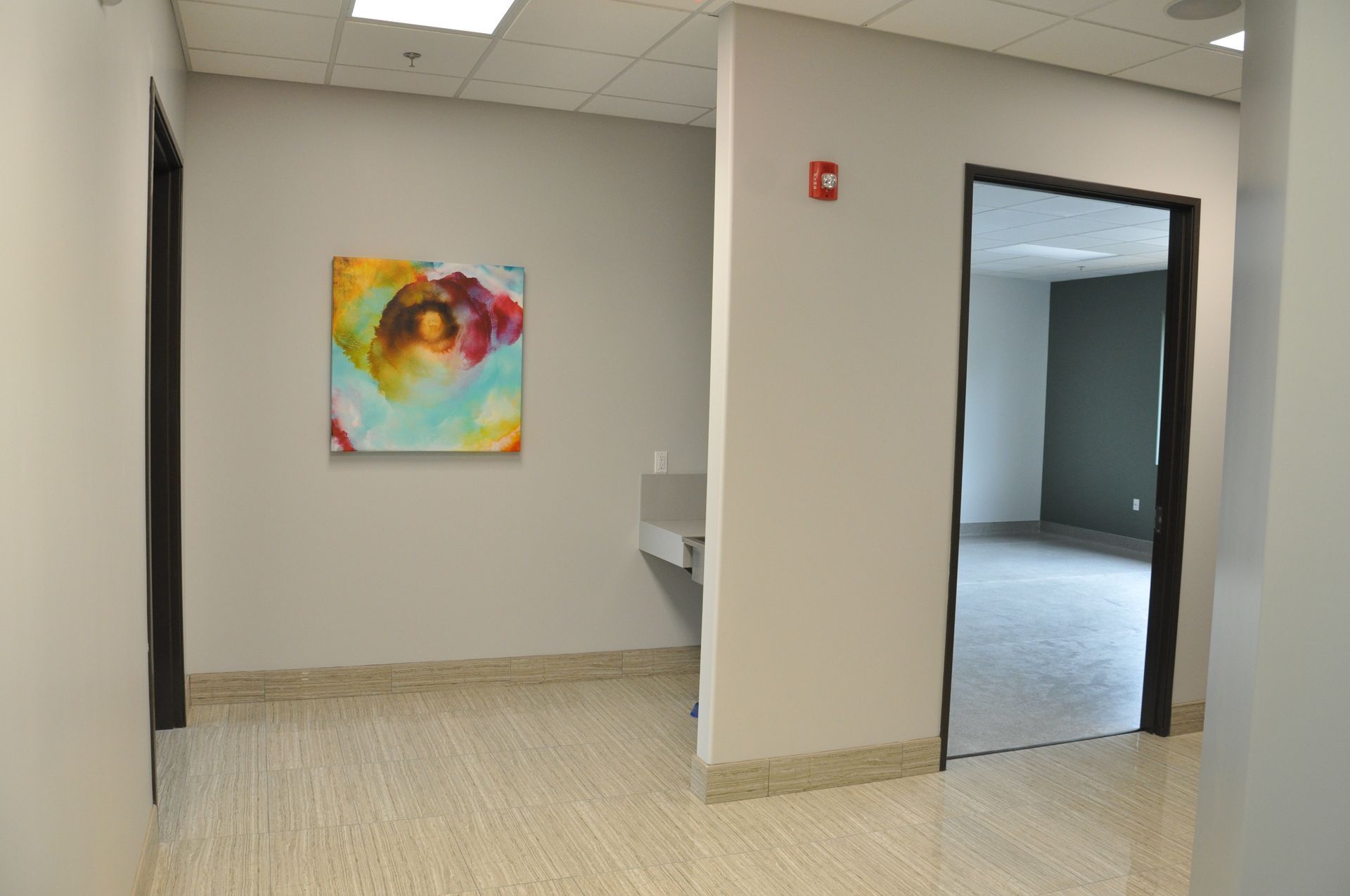 Hallway with artwork, doorway on the right, and another doorway on the left. Beige flooring and gray walls.