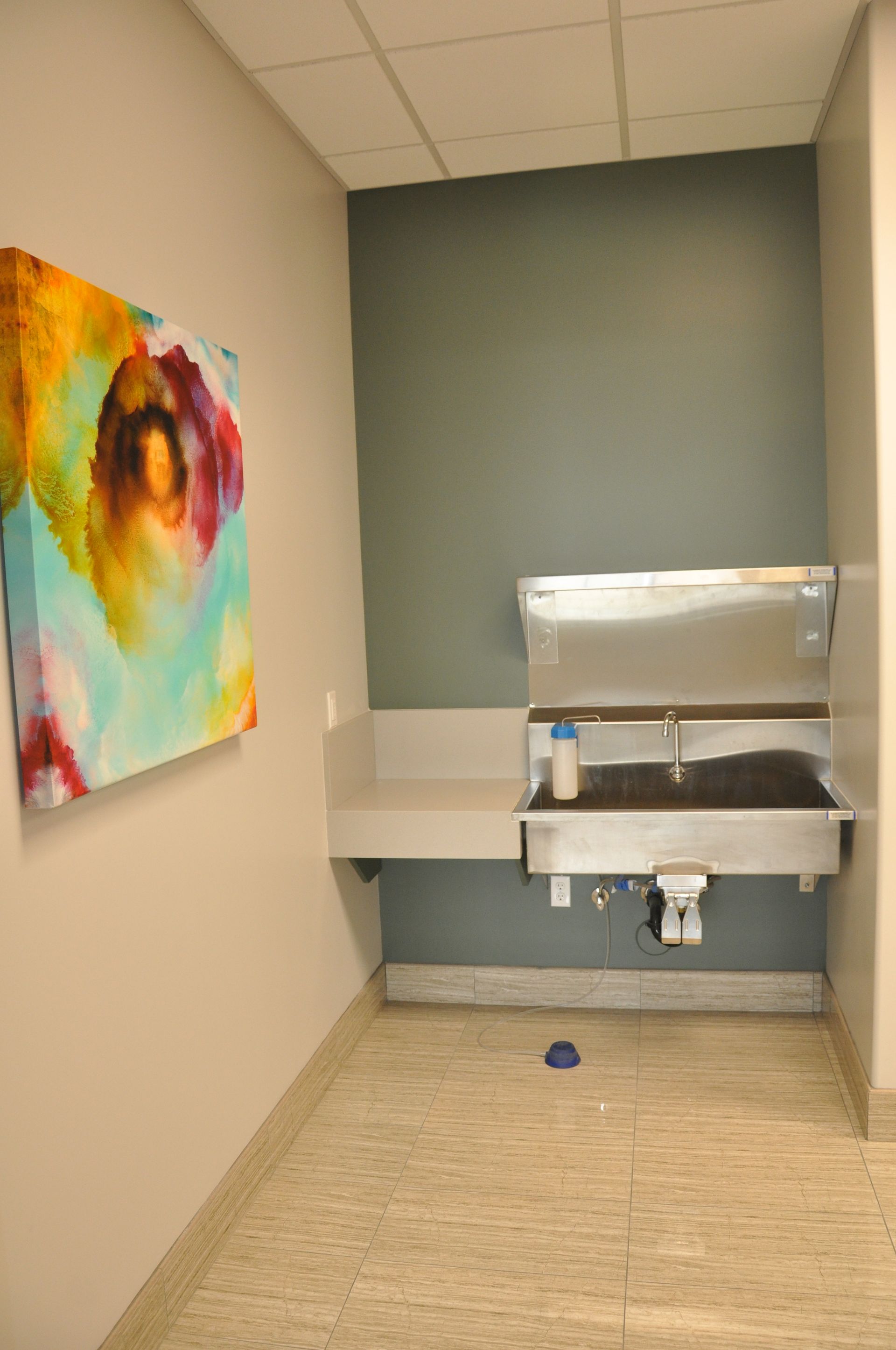 A stainless steel hand washing station on a pale green wall with colorful art and a light floor.
