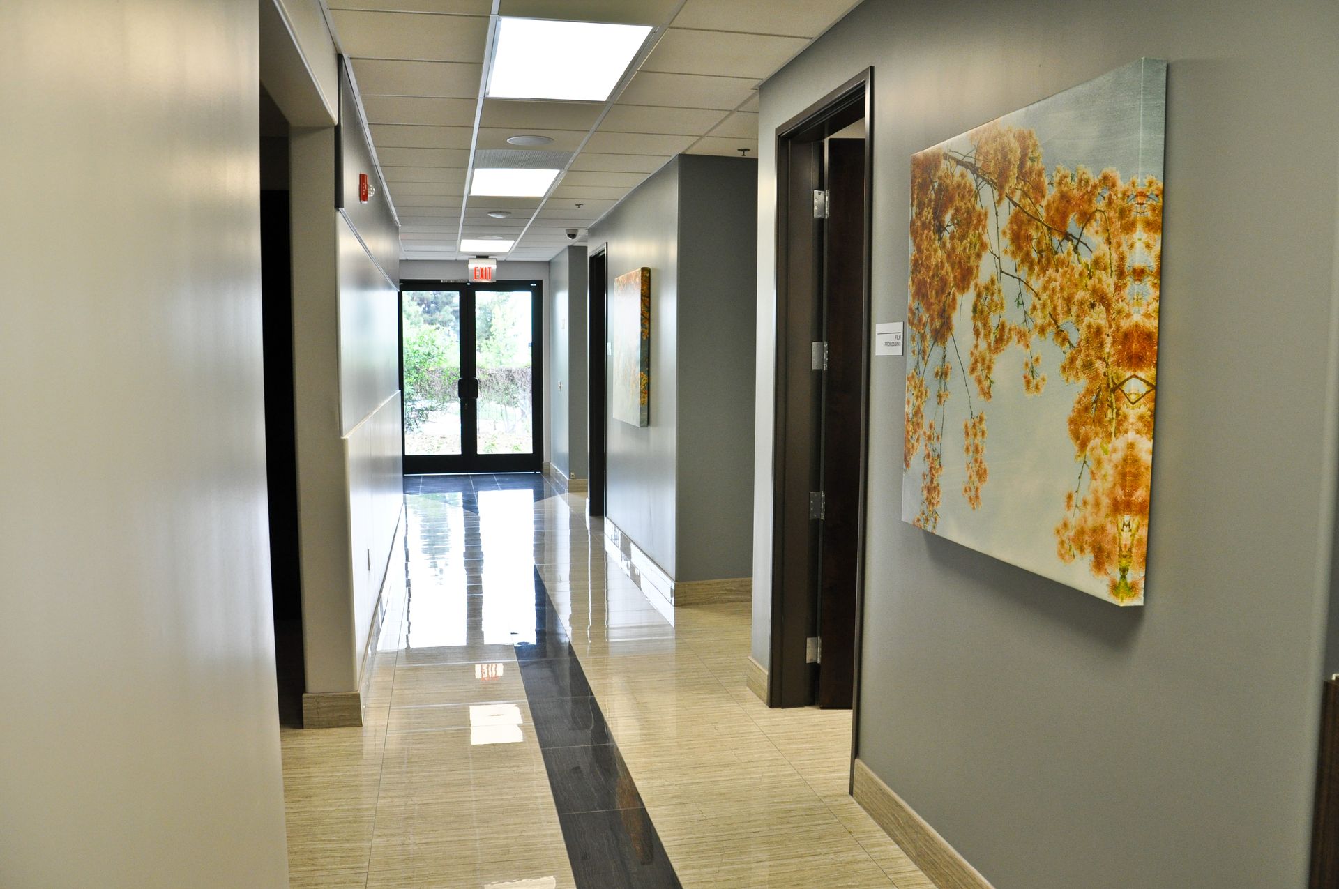 Hallway with gray walls, art, shiny floor, and doors leading to outside.