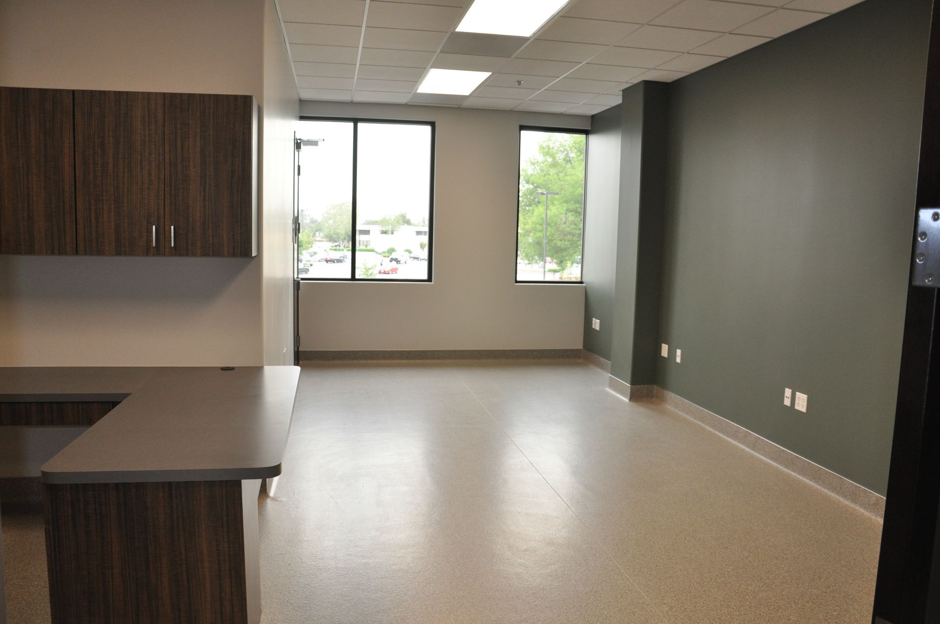 Empty office with brown cabinets, gray countertop, windows, and green accent wall.