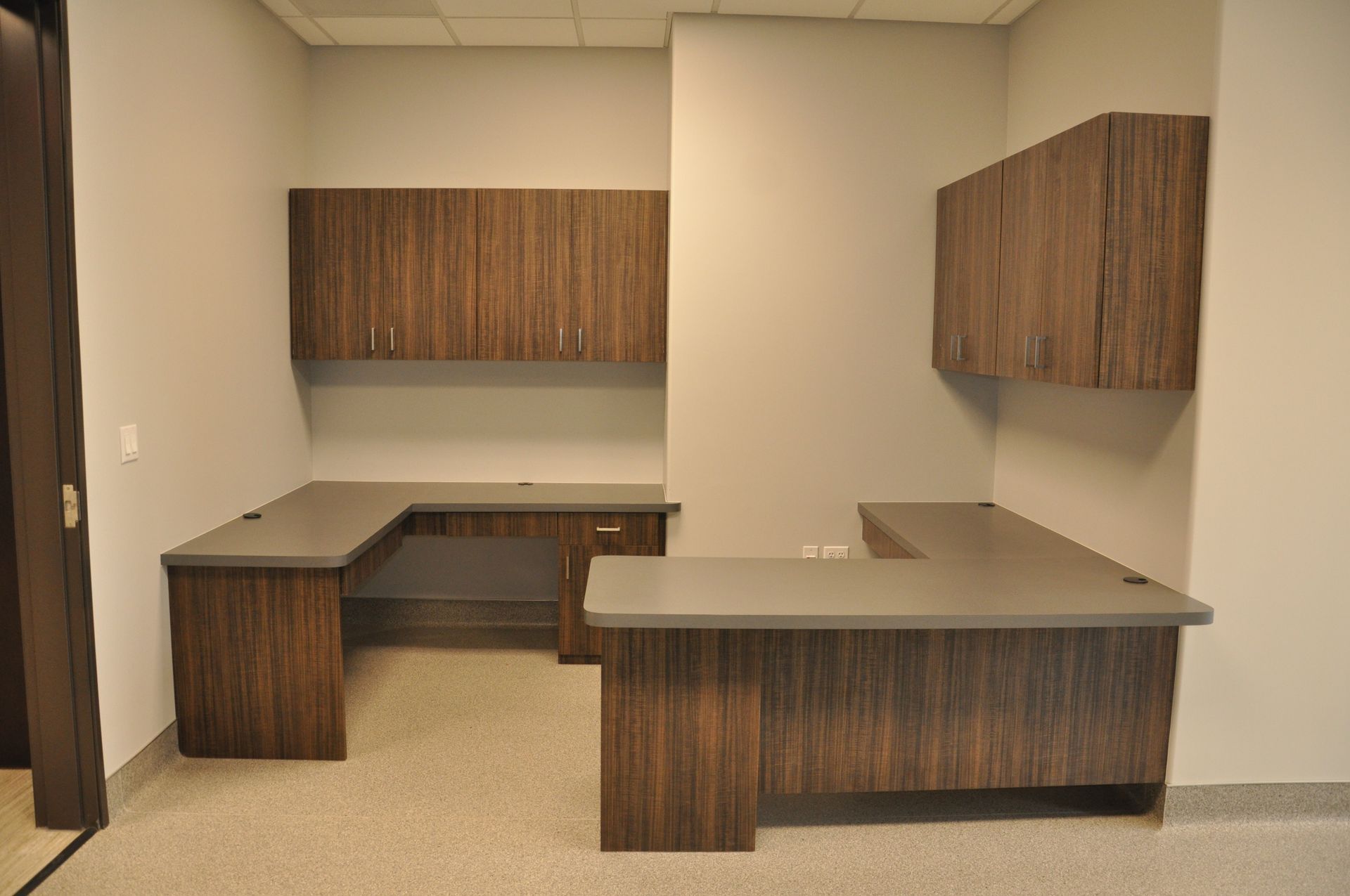 Office with brown wood desk and cabinets, light gray walls, and light speckled floor.