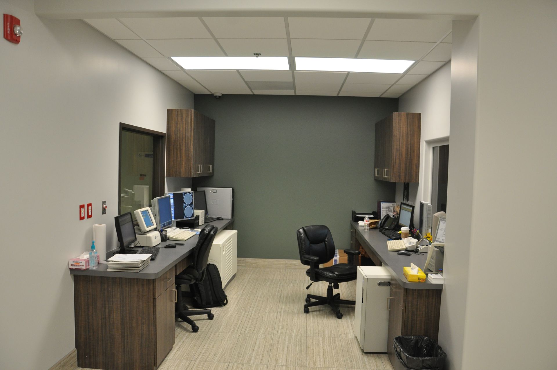 Narrow office hallway with two workstations, dark wood cabinets, and gray walls.