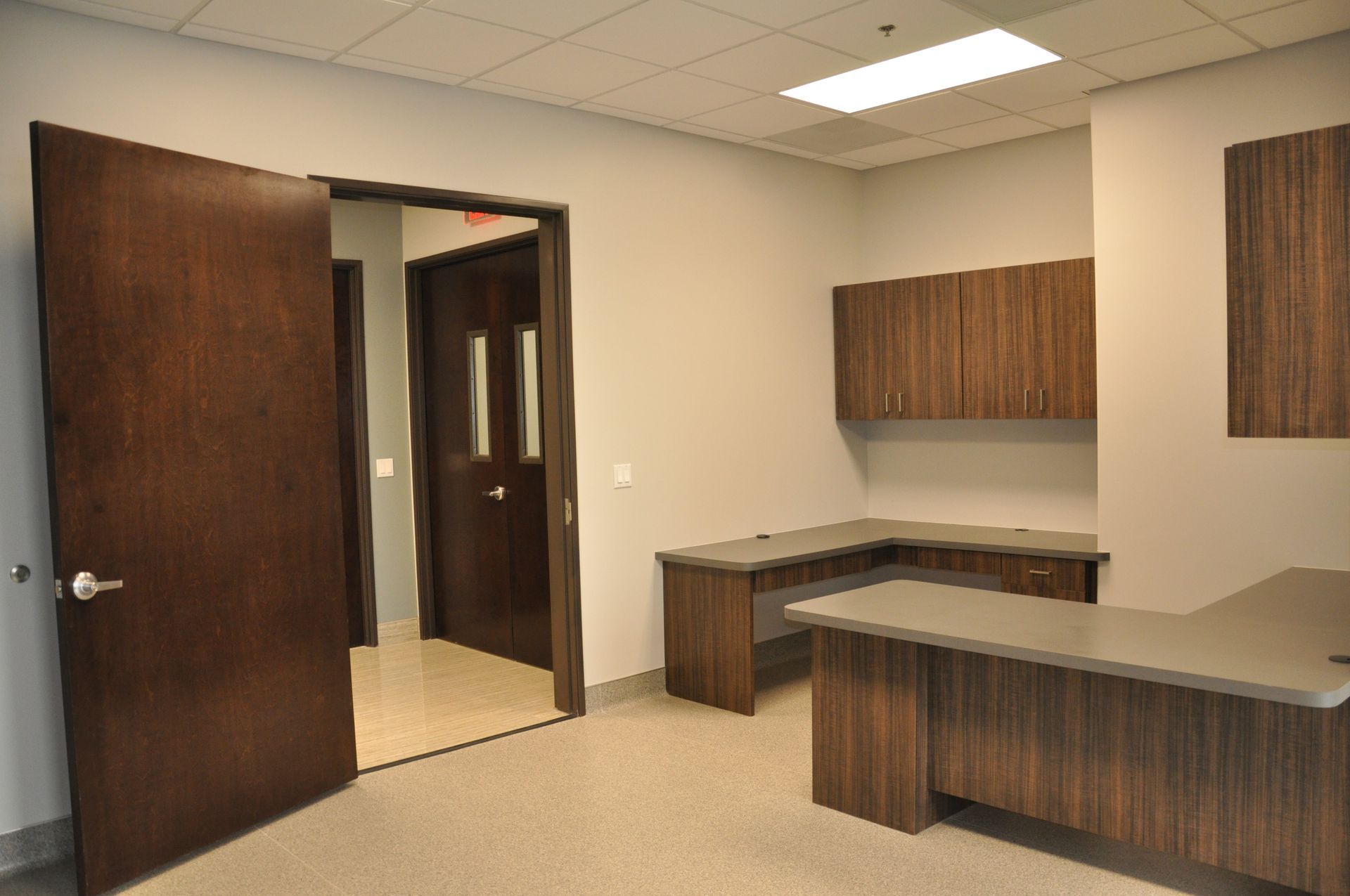 Office interior with desk, dark wood cabinets and doors, gray walls.