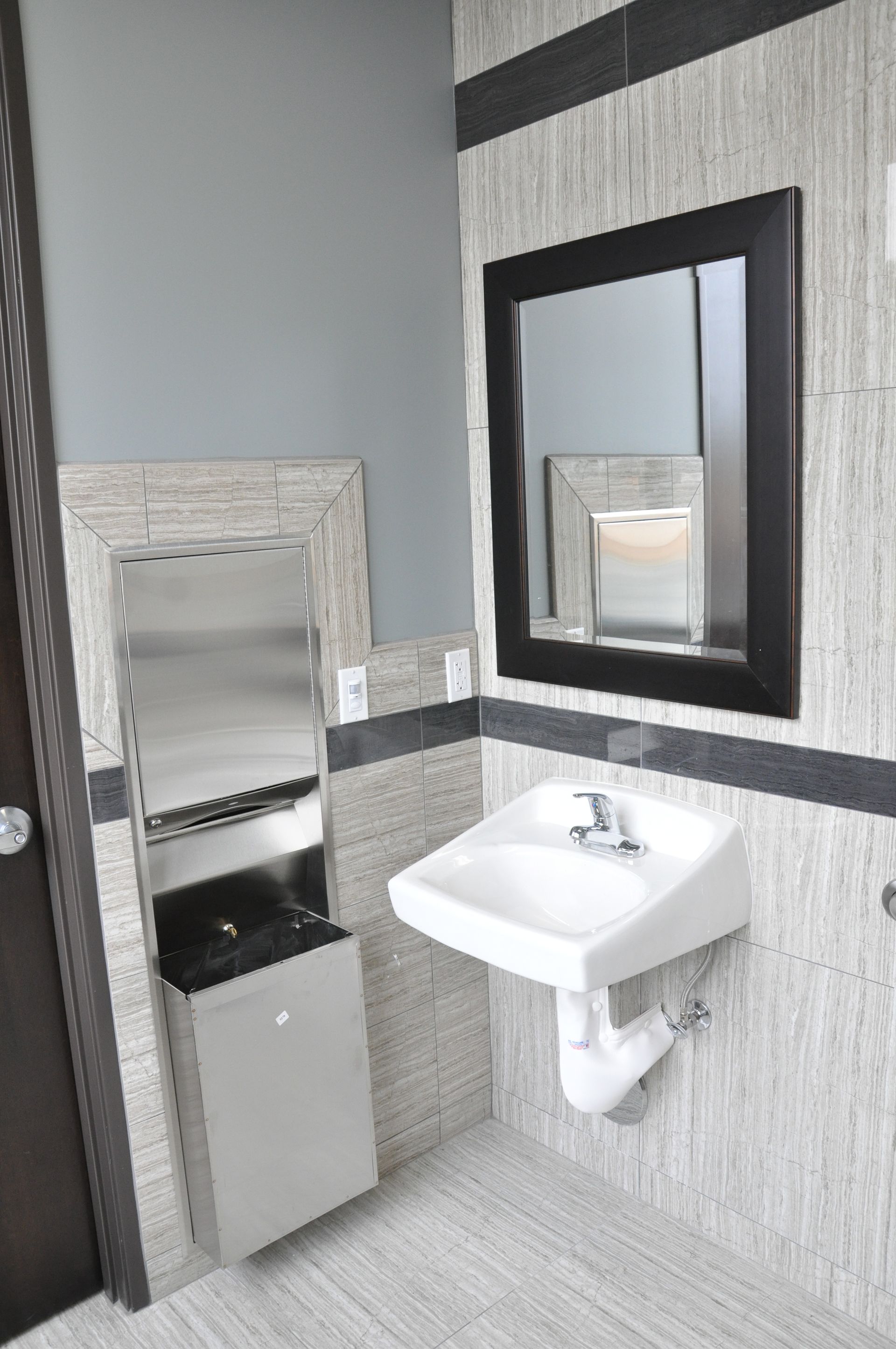 Accessible restroom with a sink, mirror, and paper towel dispenser on a textured wall.