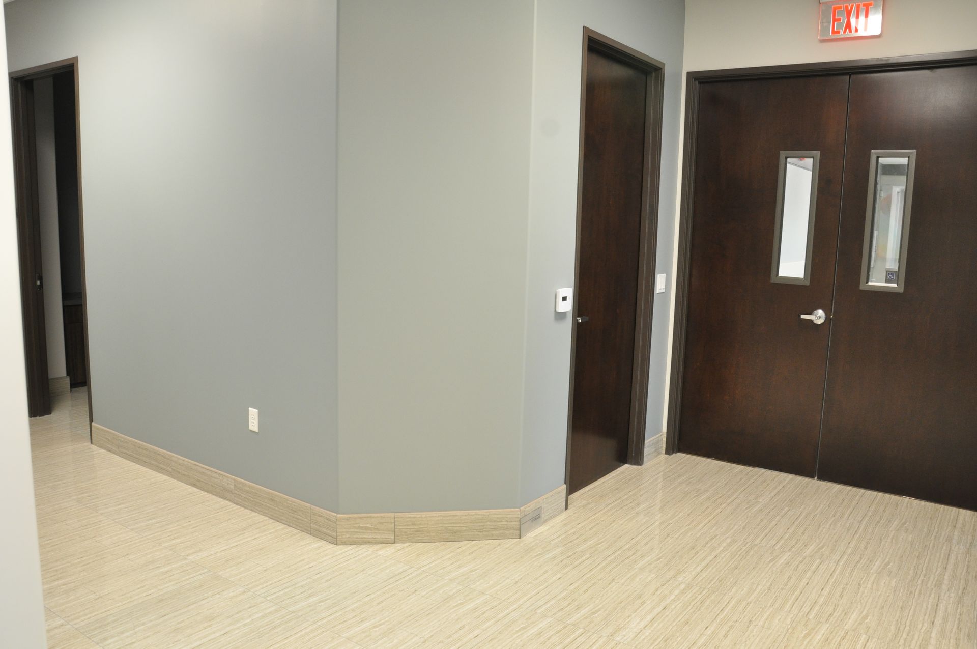Hallway with grey walls, beige flooring, and a few dark brown doors.