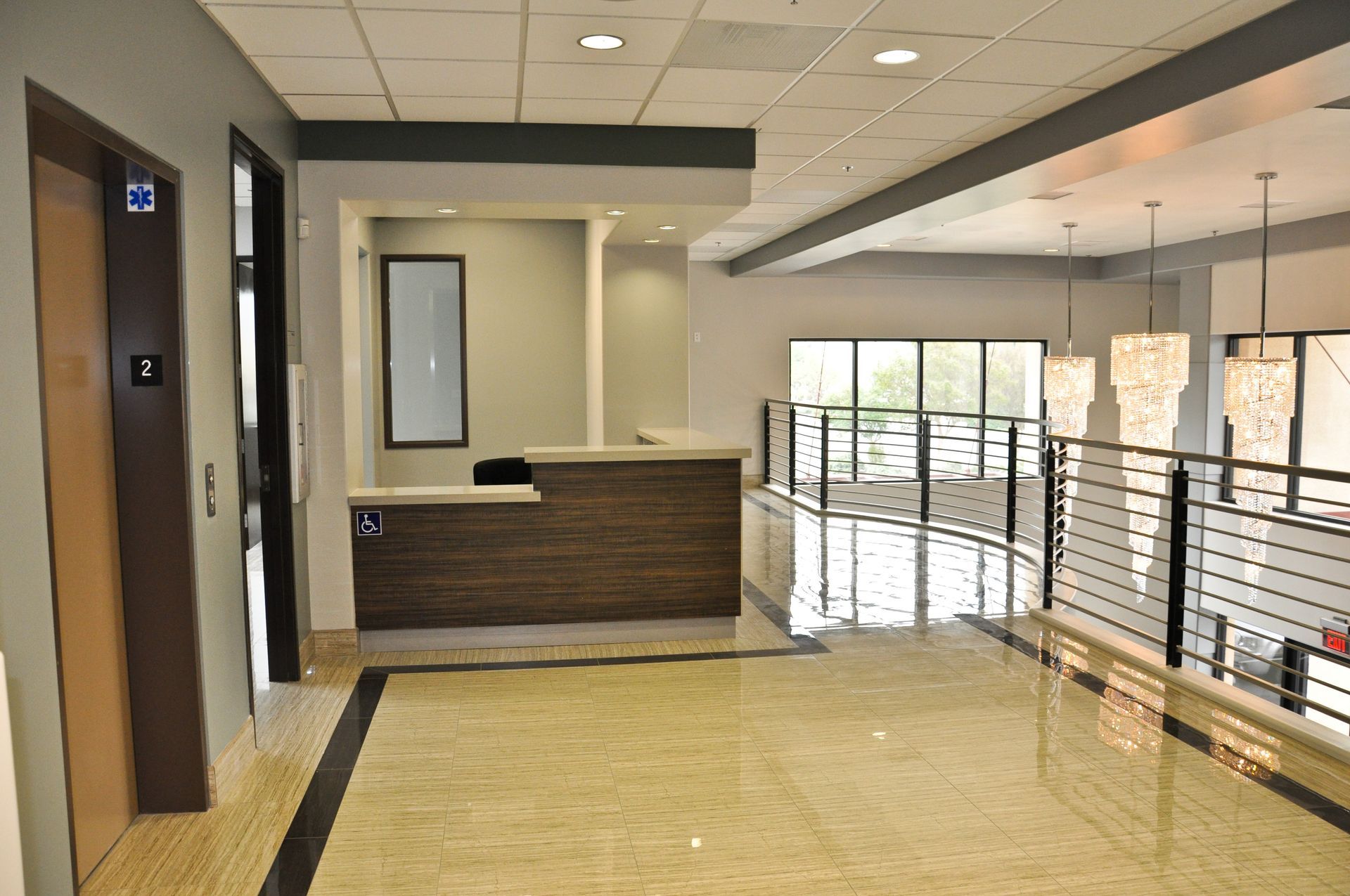 Lobby with a reception desk, elevator, and a second-floor railing. Neutral colors dominate the space.