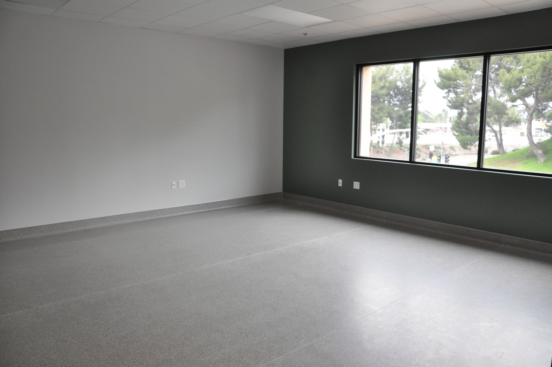 Empty room with gray floor, two-tone walls (gray and dark green), and a window.