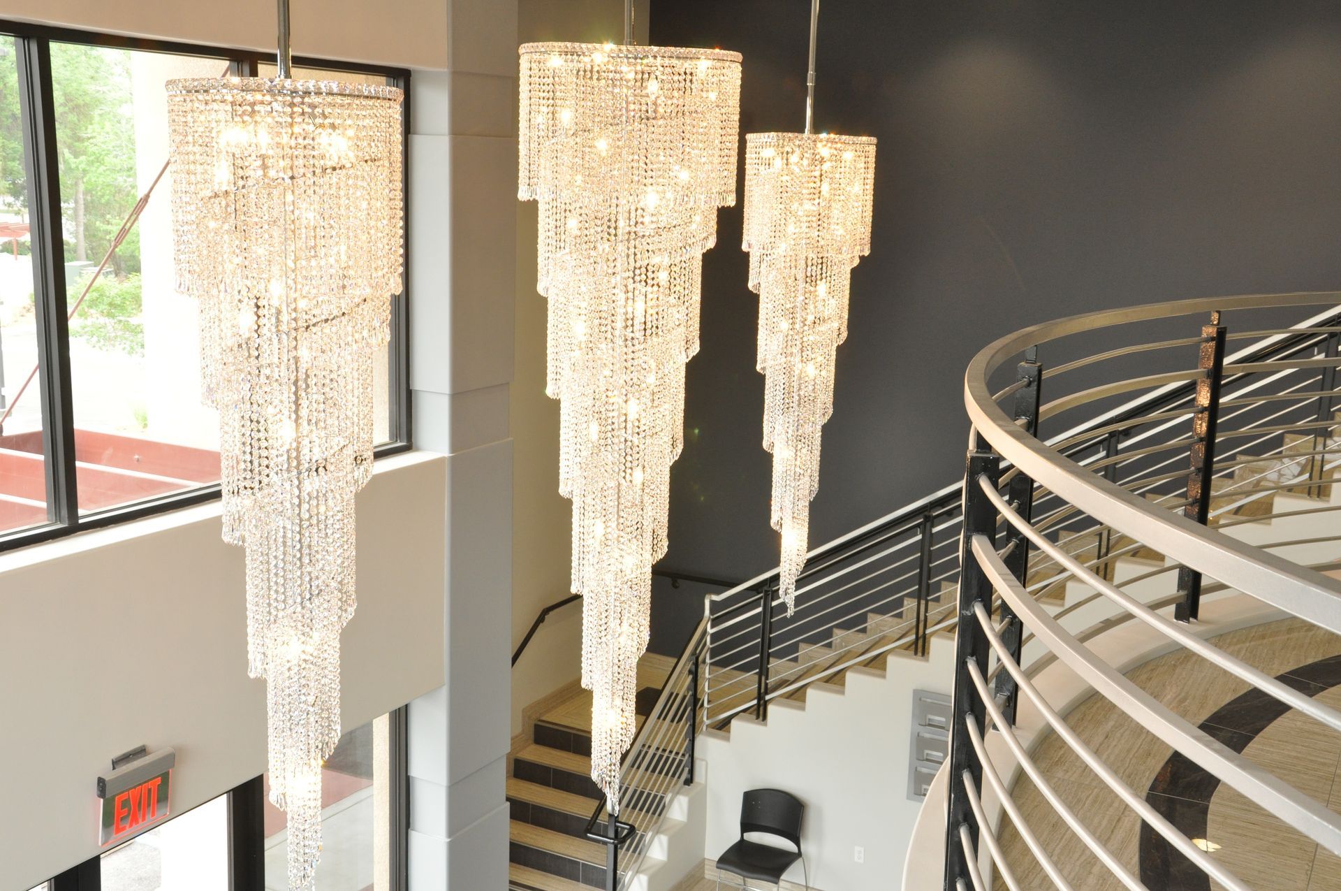 Three tiered crystal chandeliers hang in a modern entryway with a staircase and curved railing.