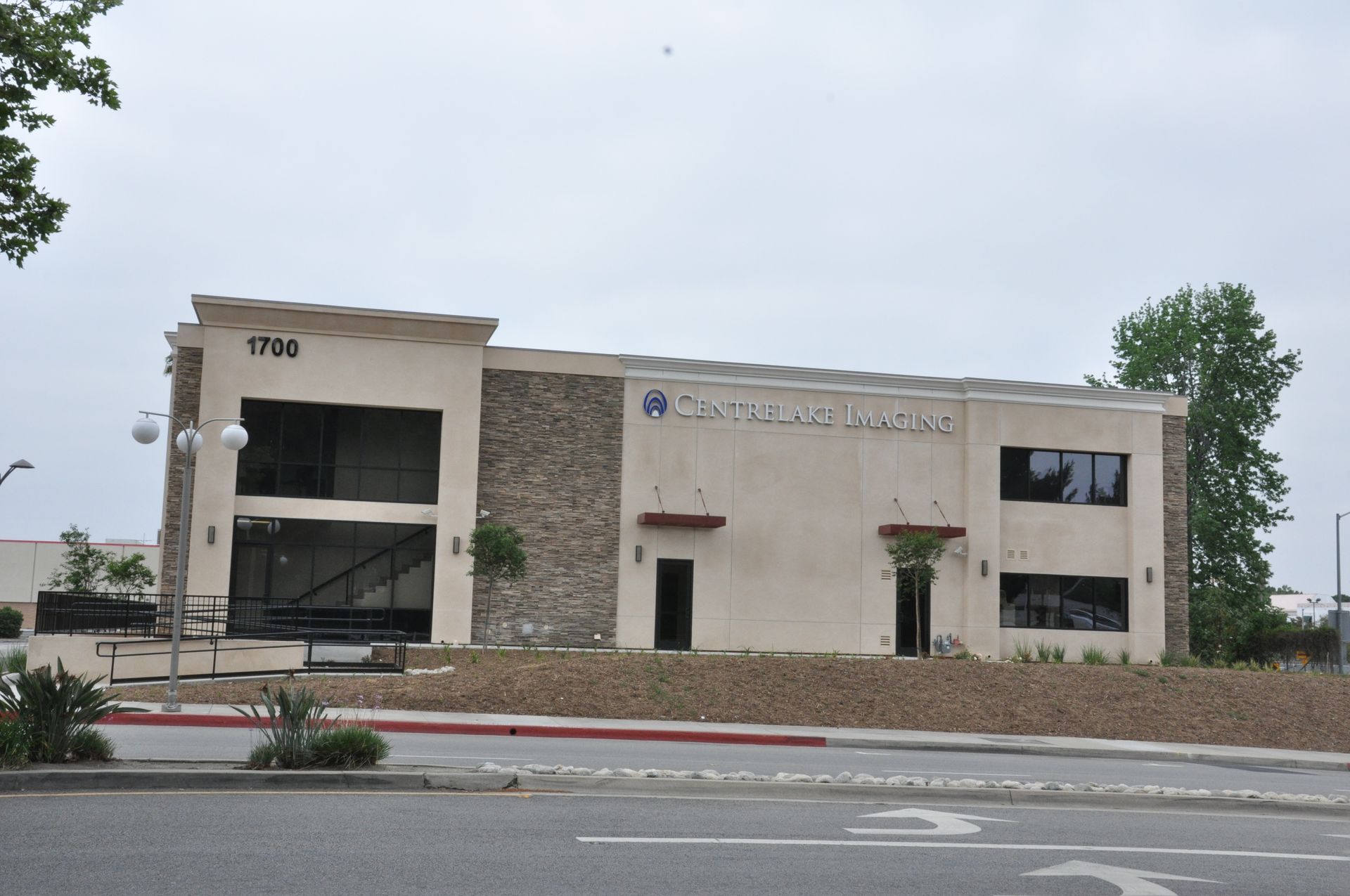 Exterior of a commercial building, tan stucco with stone accents, under a cloudy sky.
