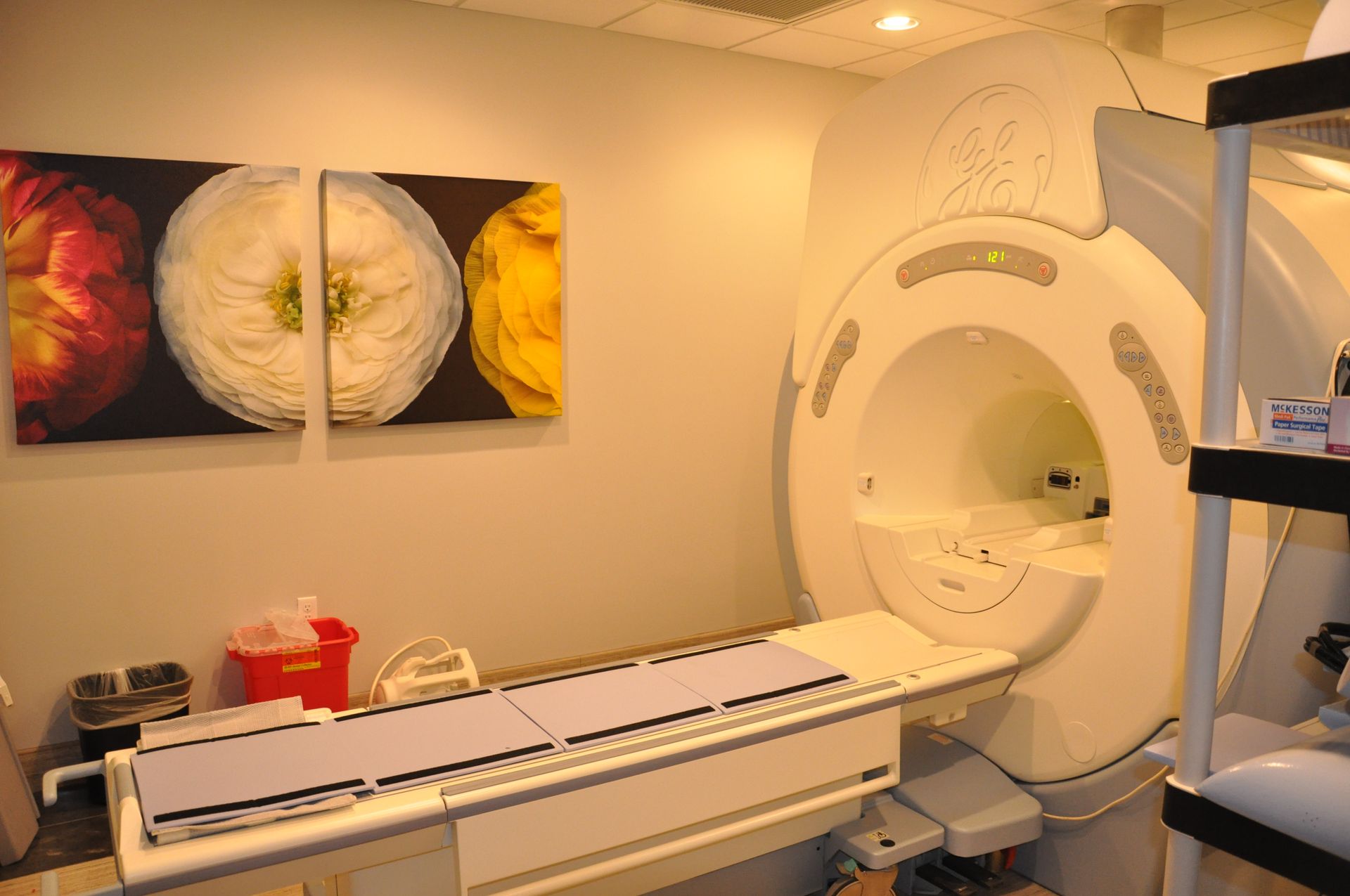 An MRI machine in a medical office; a patient bed is extended, artwork on the wall.
