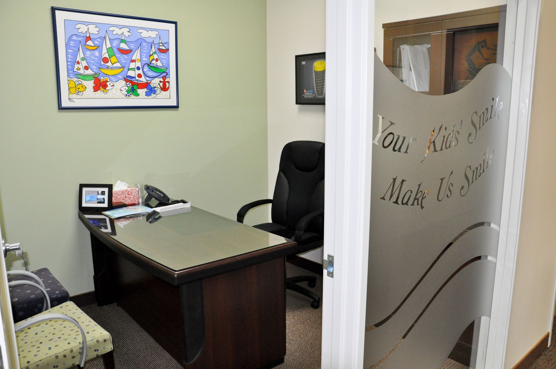 Small office with desk, chair, and artwork on the wall, visible through a frosted glass door with text.