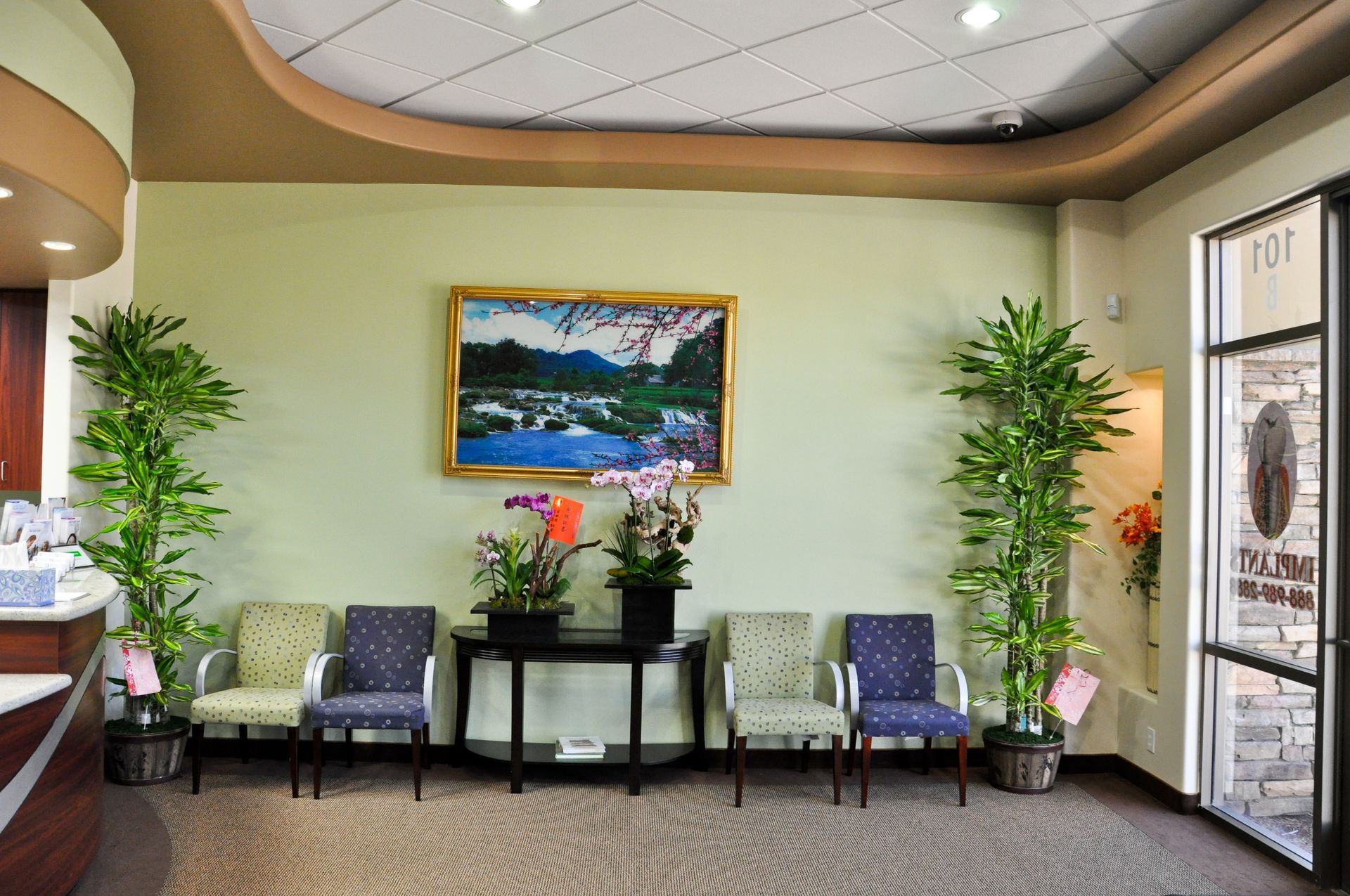 Dental office waiting room with chairs, plants, artwork, and a black table.