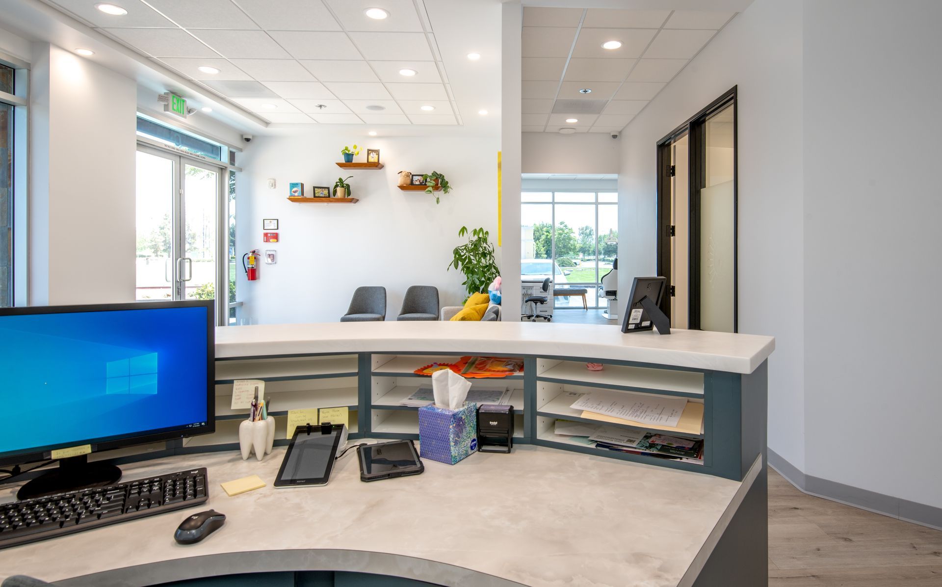 Reception desk with computer, waiting area with chairs, and open door to exterior.