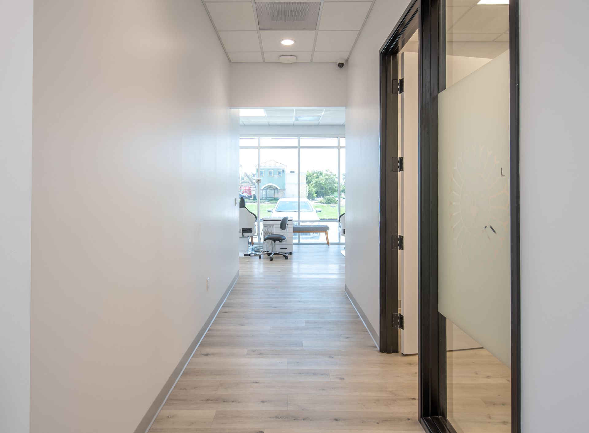 Hallway with white walls, light wood floor, and door leading to a room with a window.