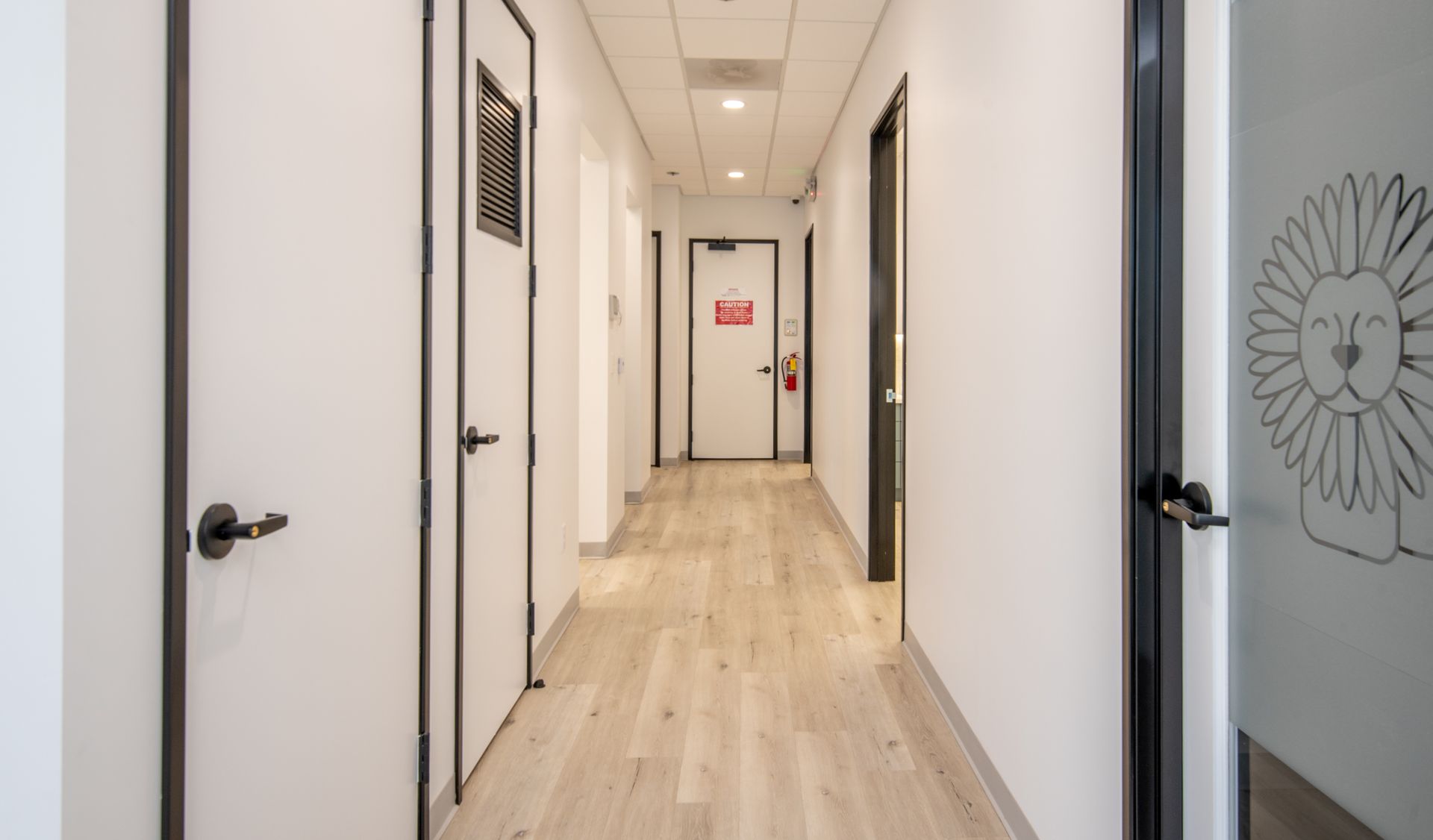 Hallway with white walls, wood floors, and black-framed doors. Lion drawing on one door.