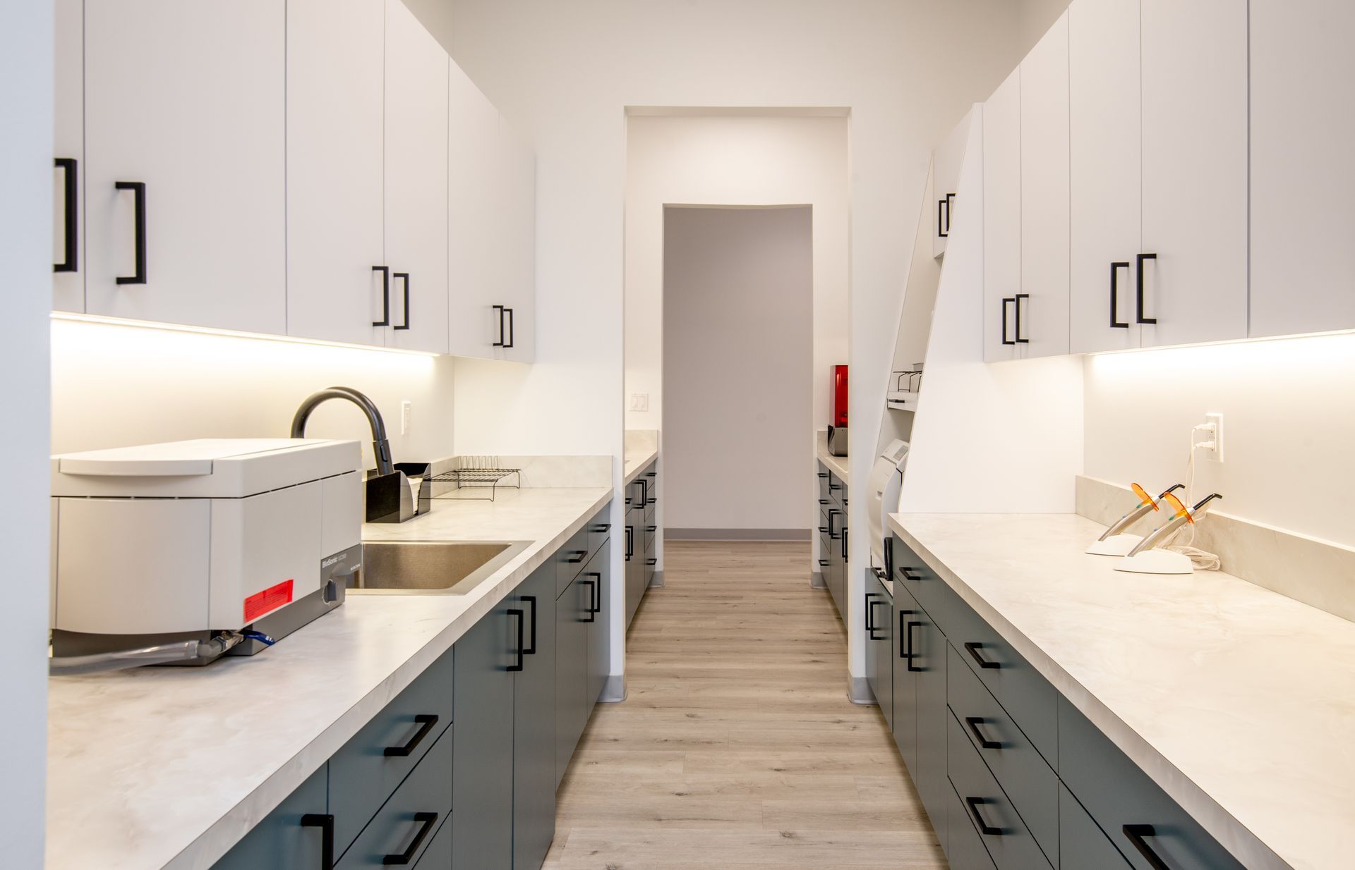 Narrow dental office lab with white and blue cabinets, stainless sink, and medical equipment.