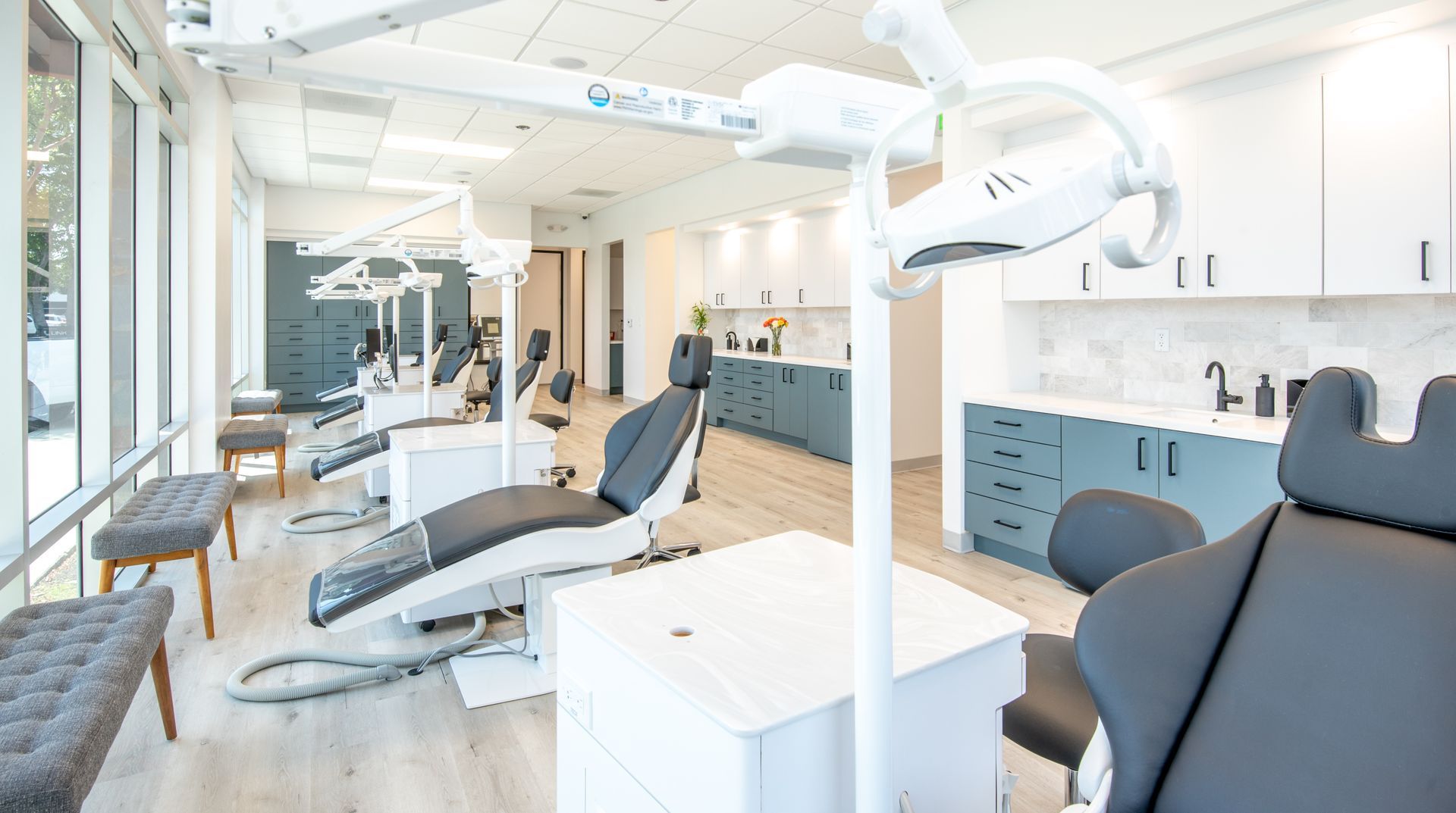 Bright, modern dental office with chairs, equipment, and teal cabinetry.