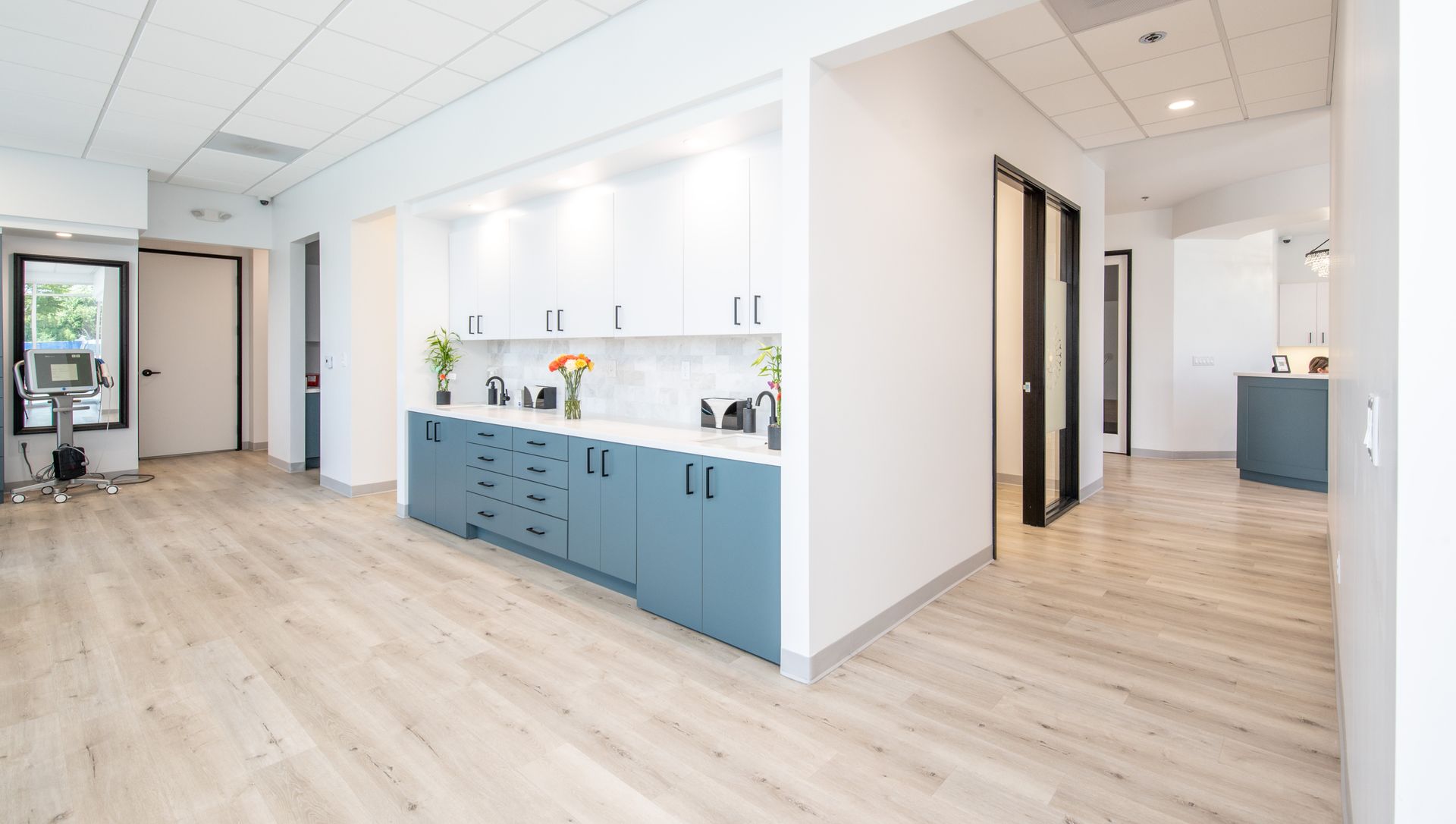 Modern office hallway with light wood floors and white and blue cabinetry.