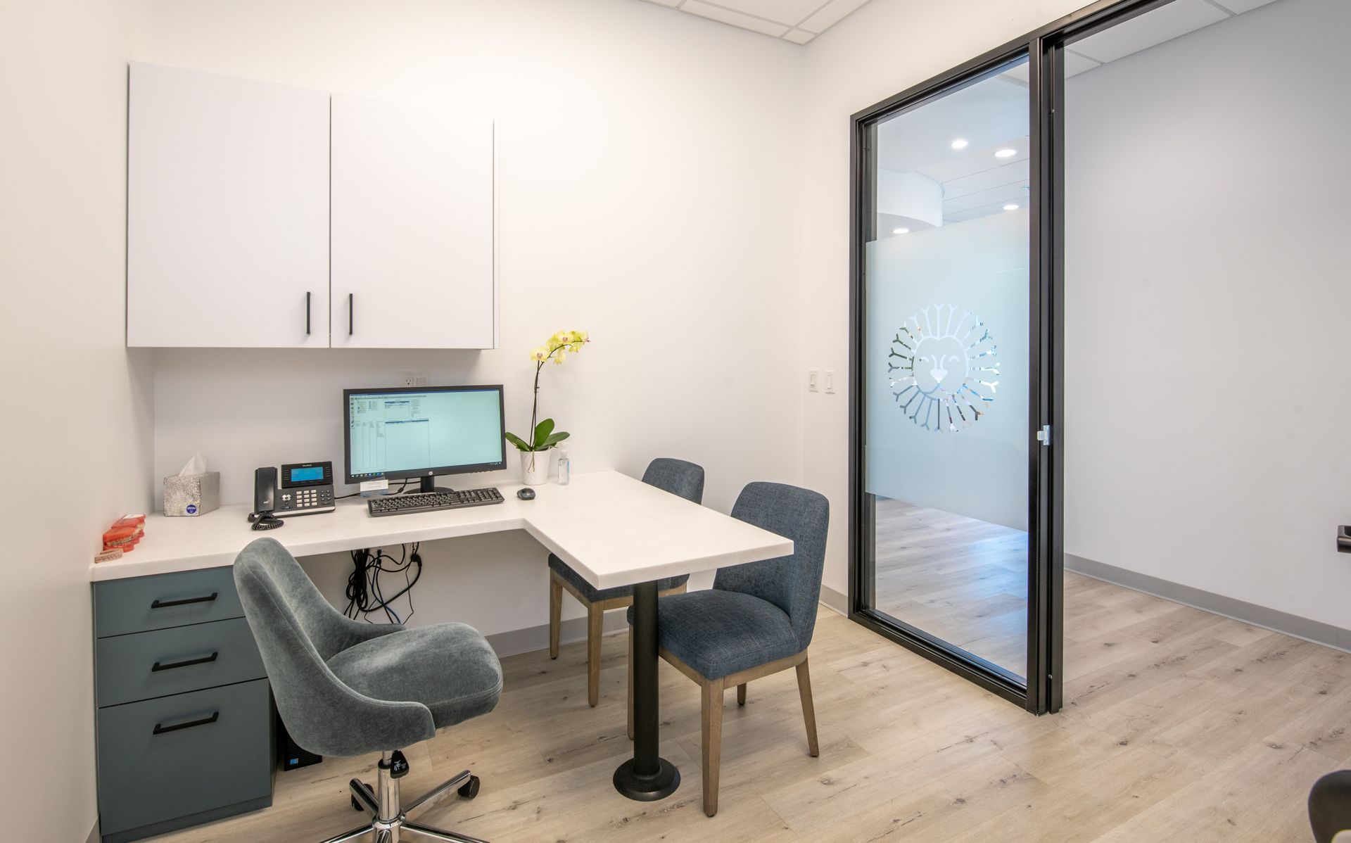 A modern office with a desk, computer, chairs, cabinets, and a glass door.