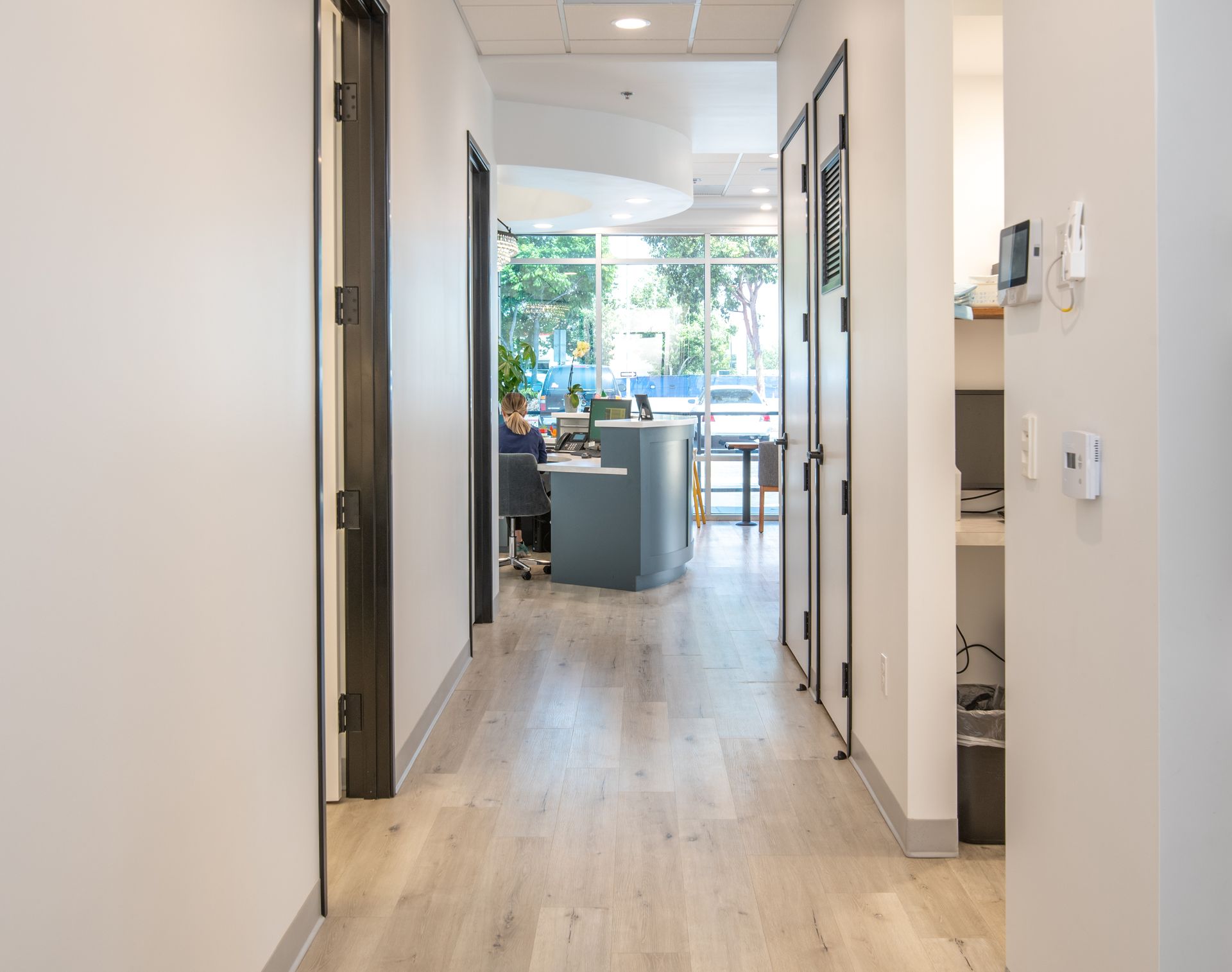 Hallway in an office; light wood floor, doors on the sides, reception desk at the end.
