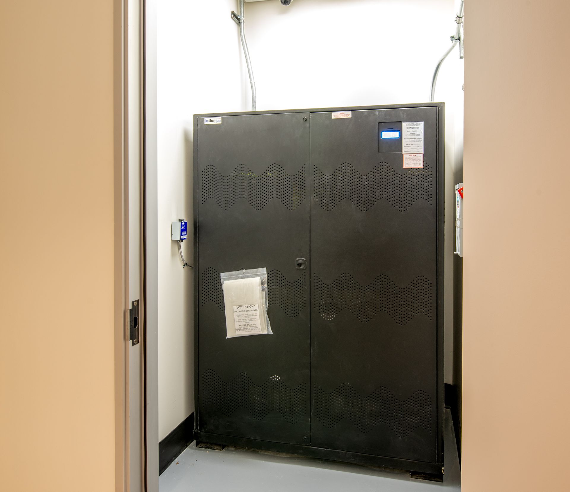 Dark metal cabinet in an alcove, possibly electrical or server equipment. Beige walls and a doorway frame the view.