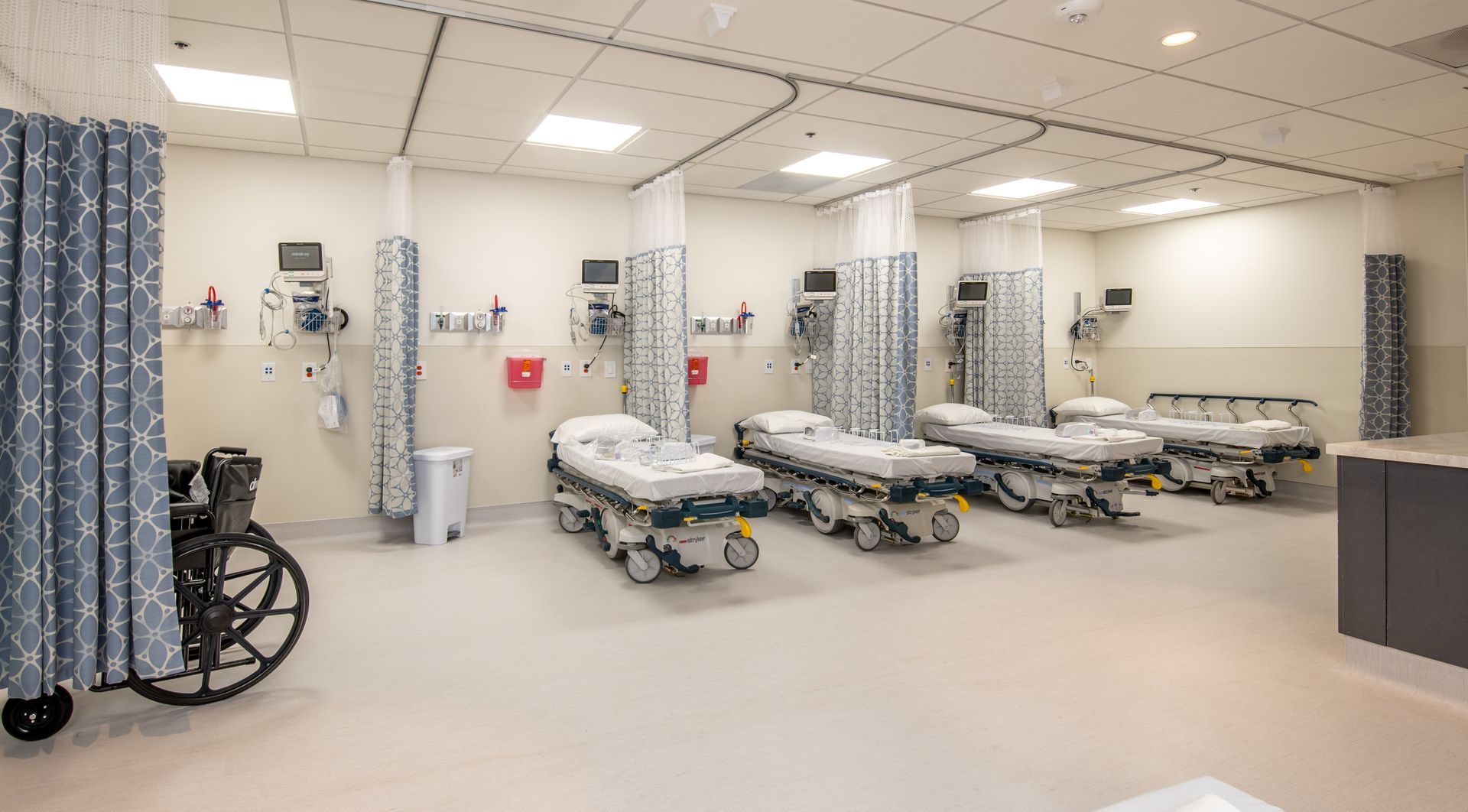 Hospital room with gurneys, medical equipment, and privacy curtains.