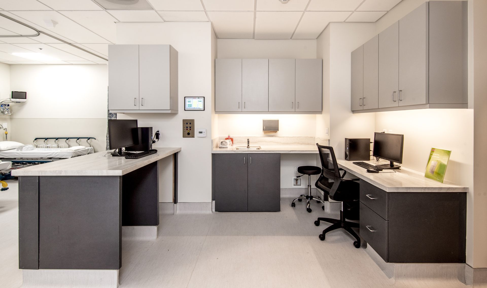 Modern medical office with gray and white cabinets, computers, and a desk chair.