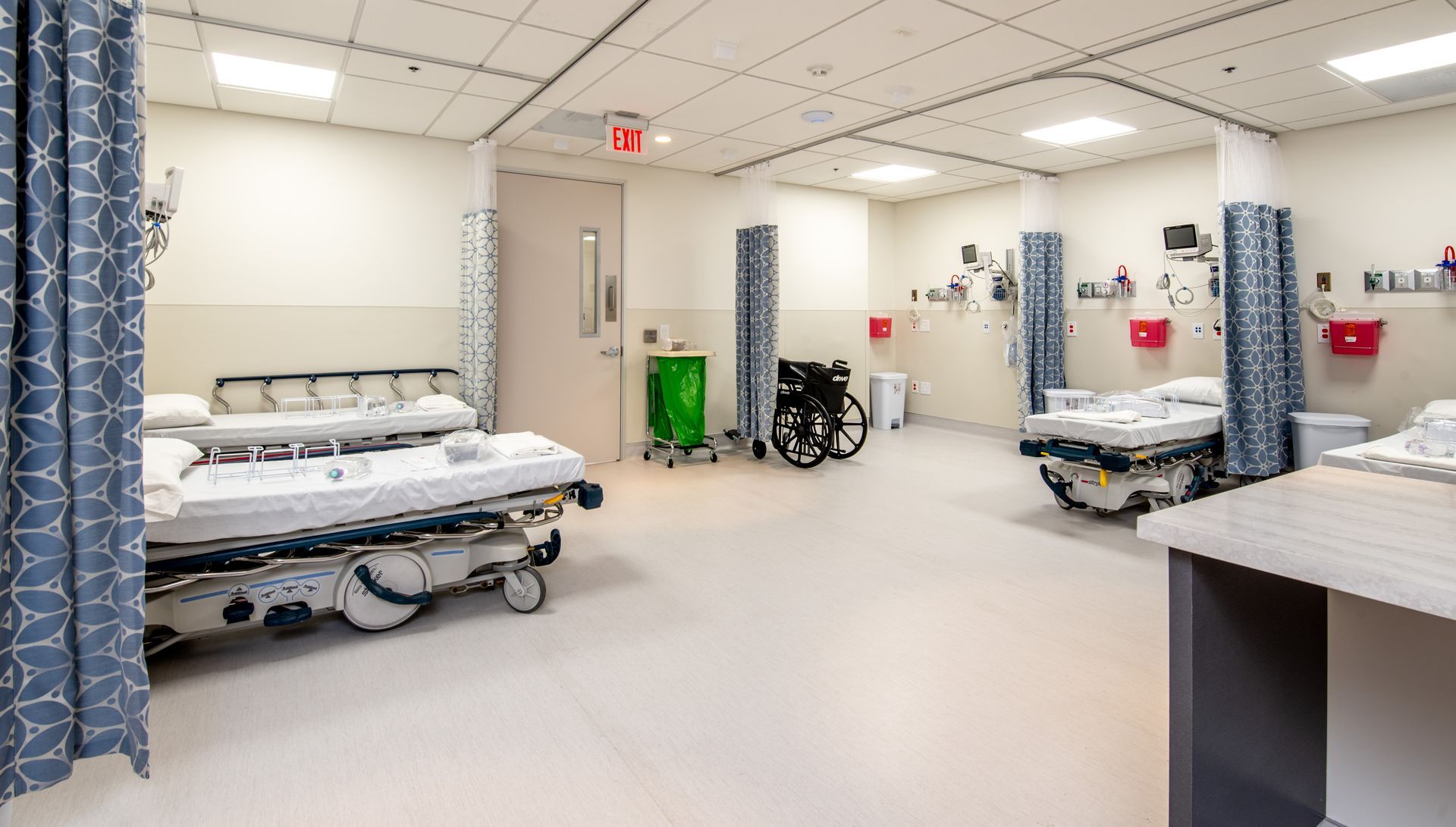 Emergency room with three beds, curtains, and medical equipment.