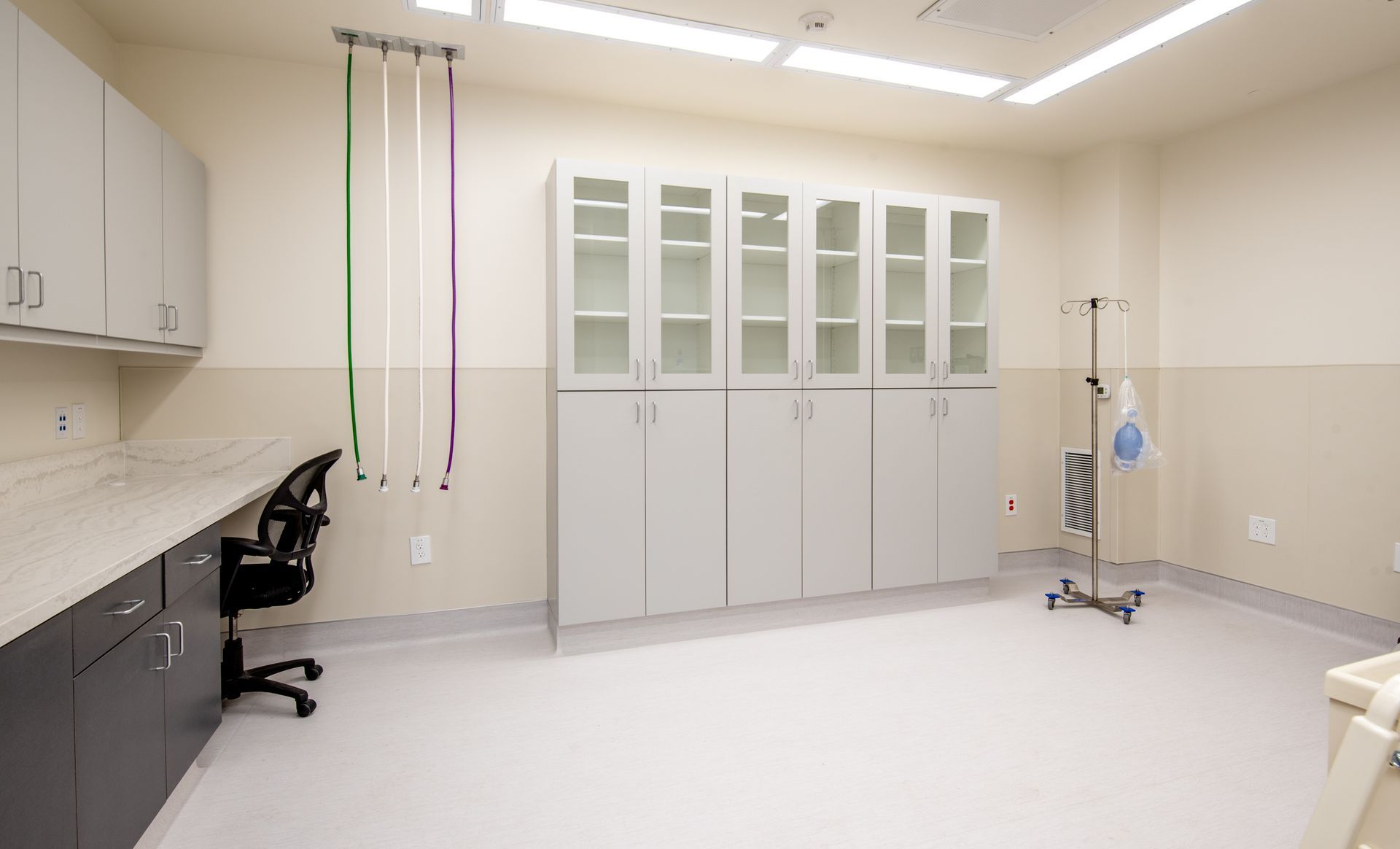 Medical exam room with cabinets, desk, and hanging cords.