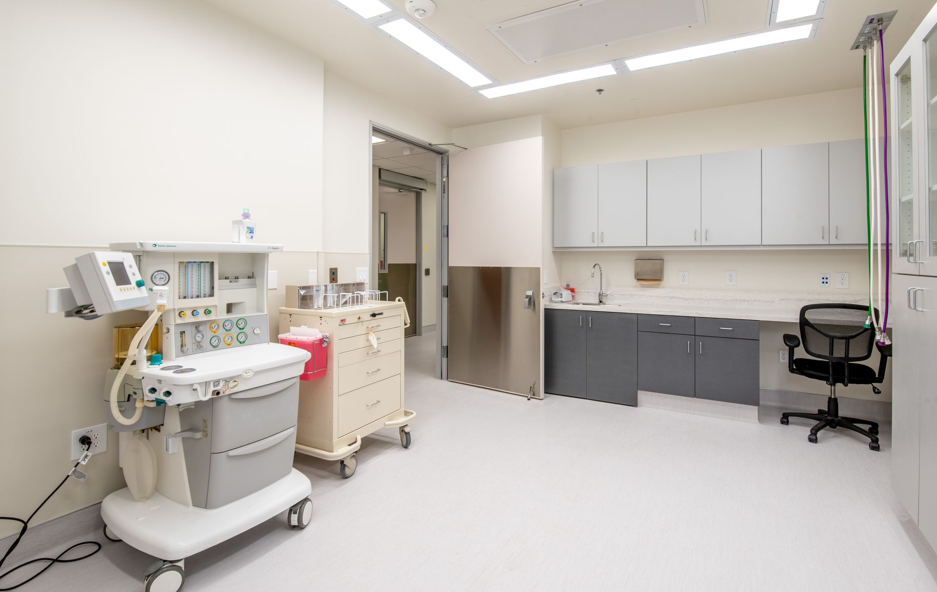An examination room with medical equipment. White walls and floor, cabinets, and a cart.