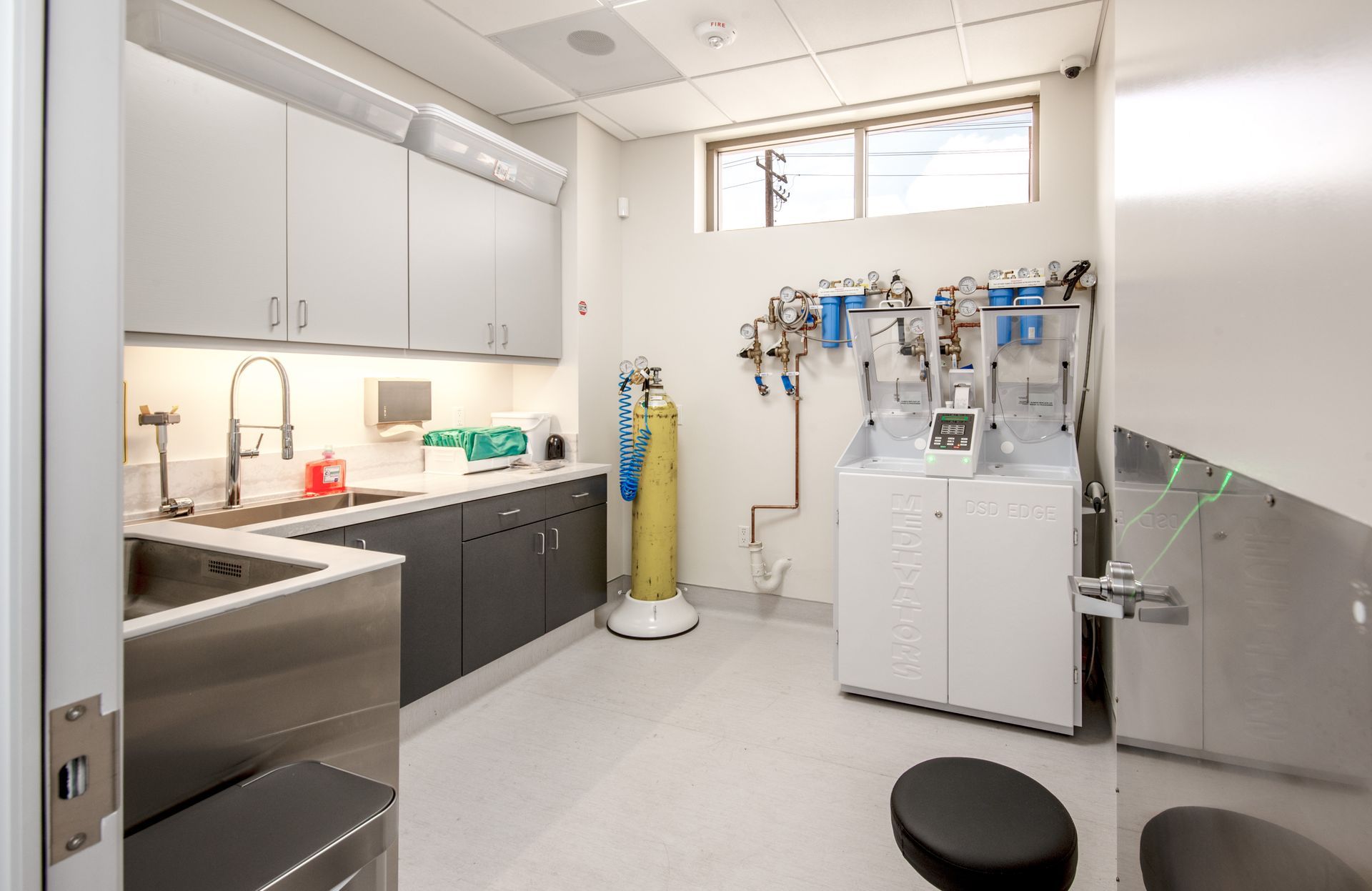 A medical room with cabinets, sink, medical equipment, and a yellow oxygen tank.
