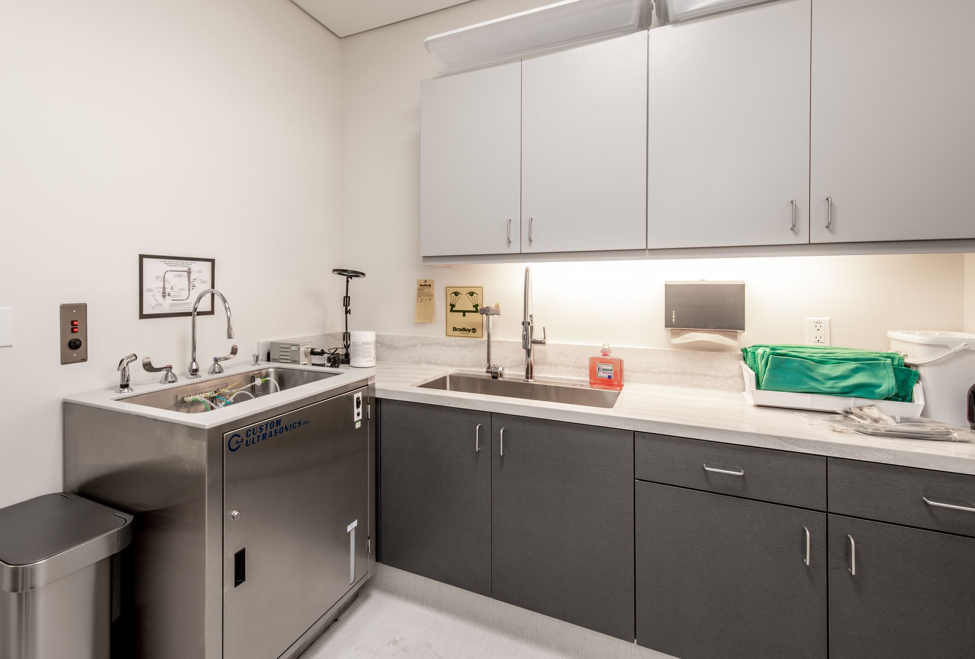 Medical room: stainless steel sink, cabinets, counter, and medical supplies against a white wall.
