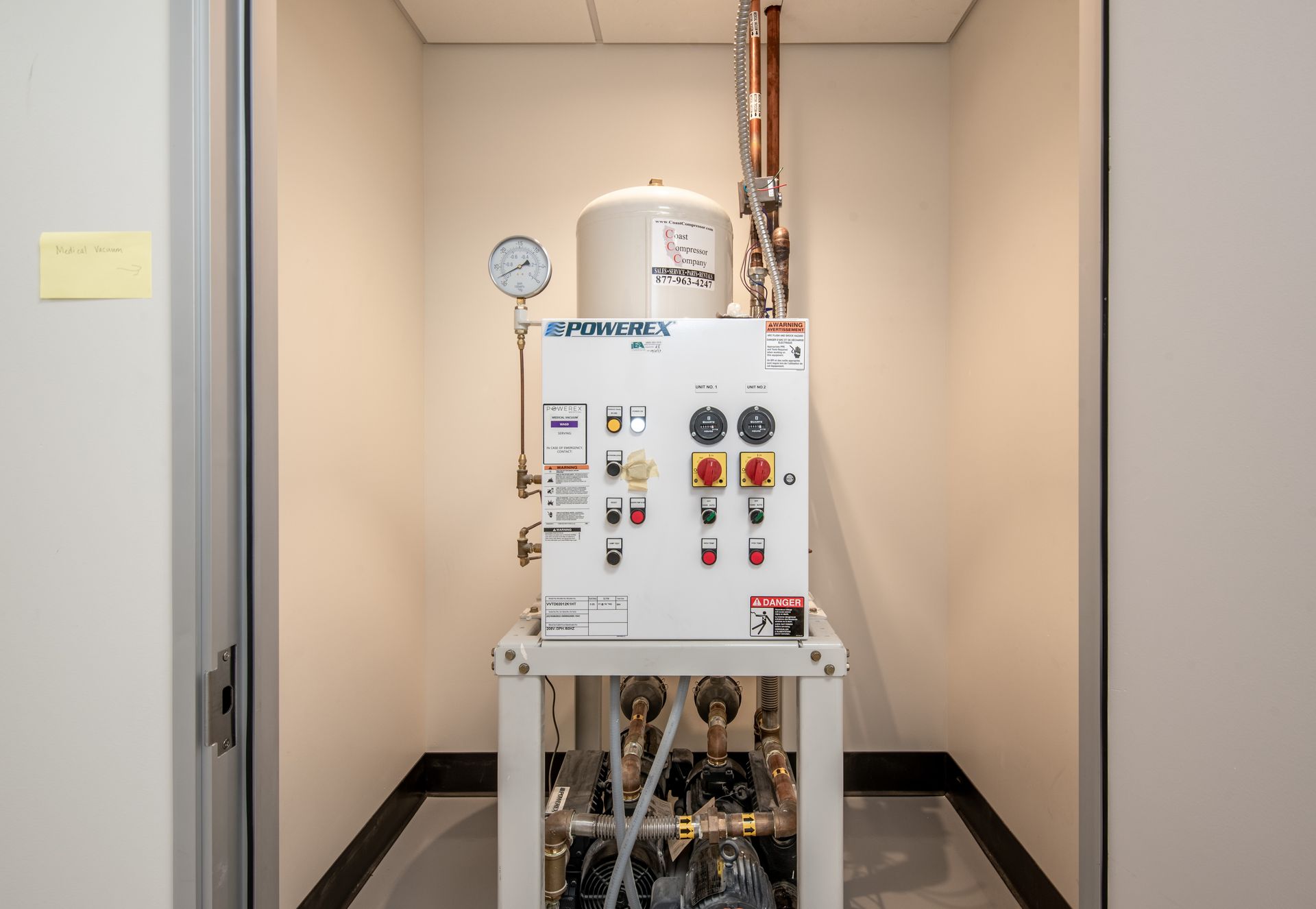 A white industrial water system in a small room with a pressure gauge and copper pipes.