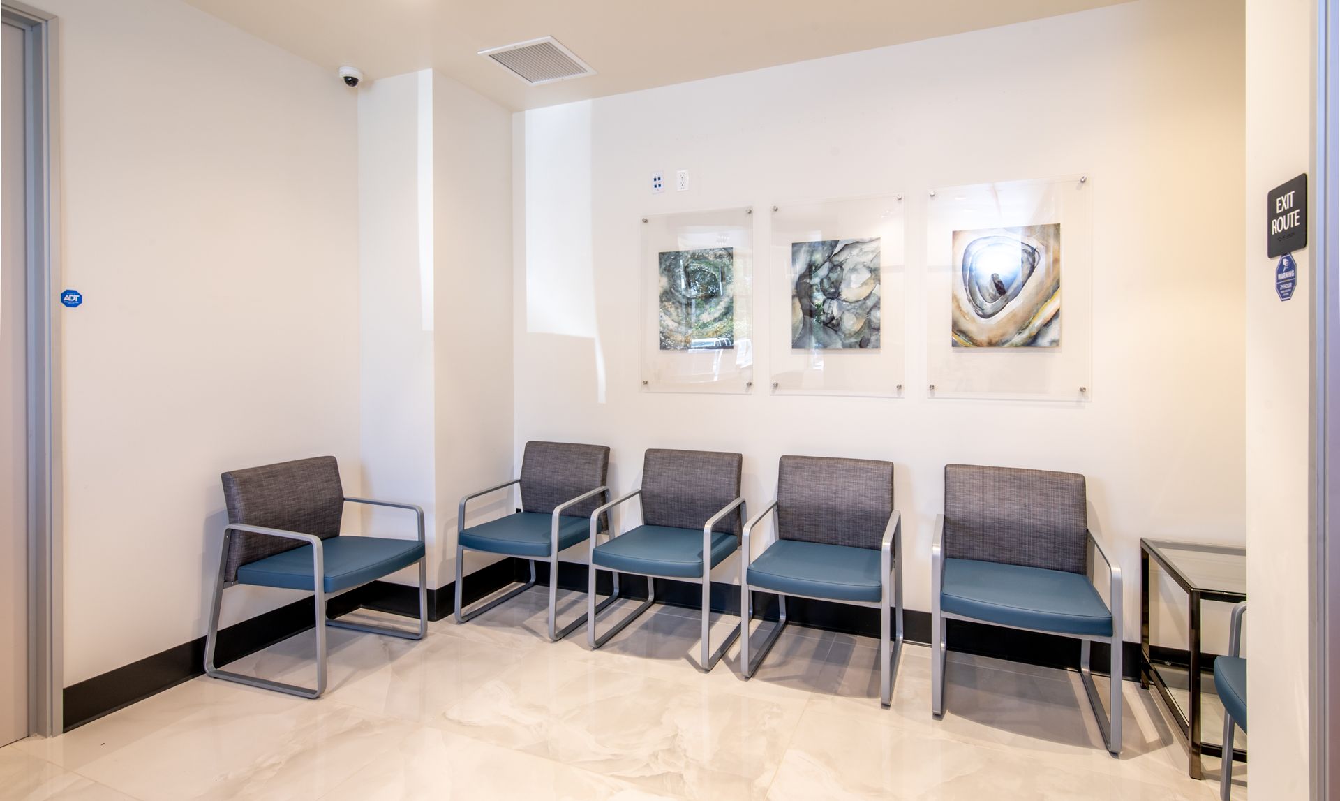 Waiting room with blue chairs, framed art, and a small side table.