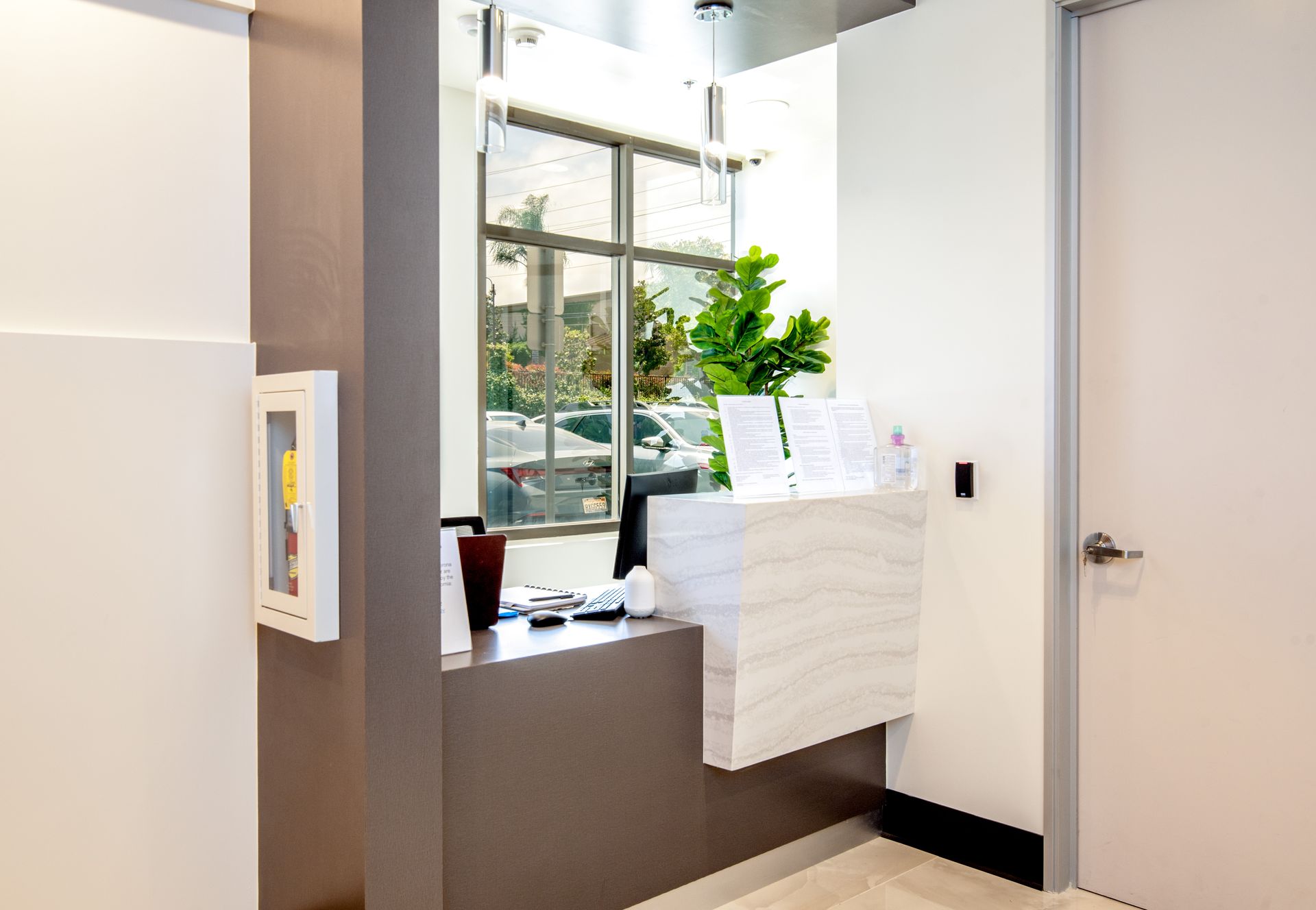 Reception desk in a modern office, with a window overlooking cars. White and gray colors dominate.
