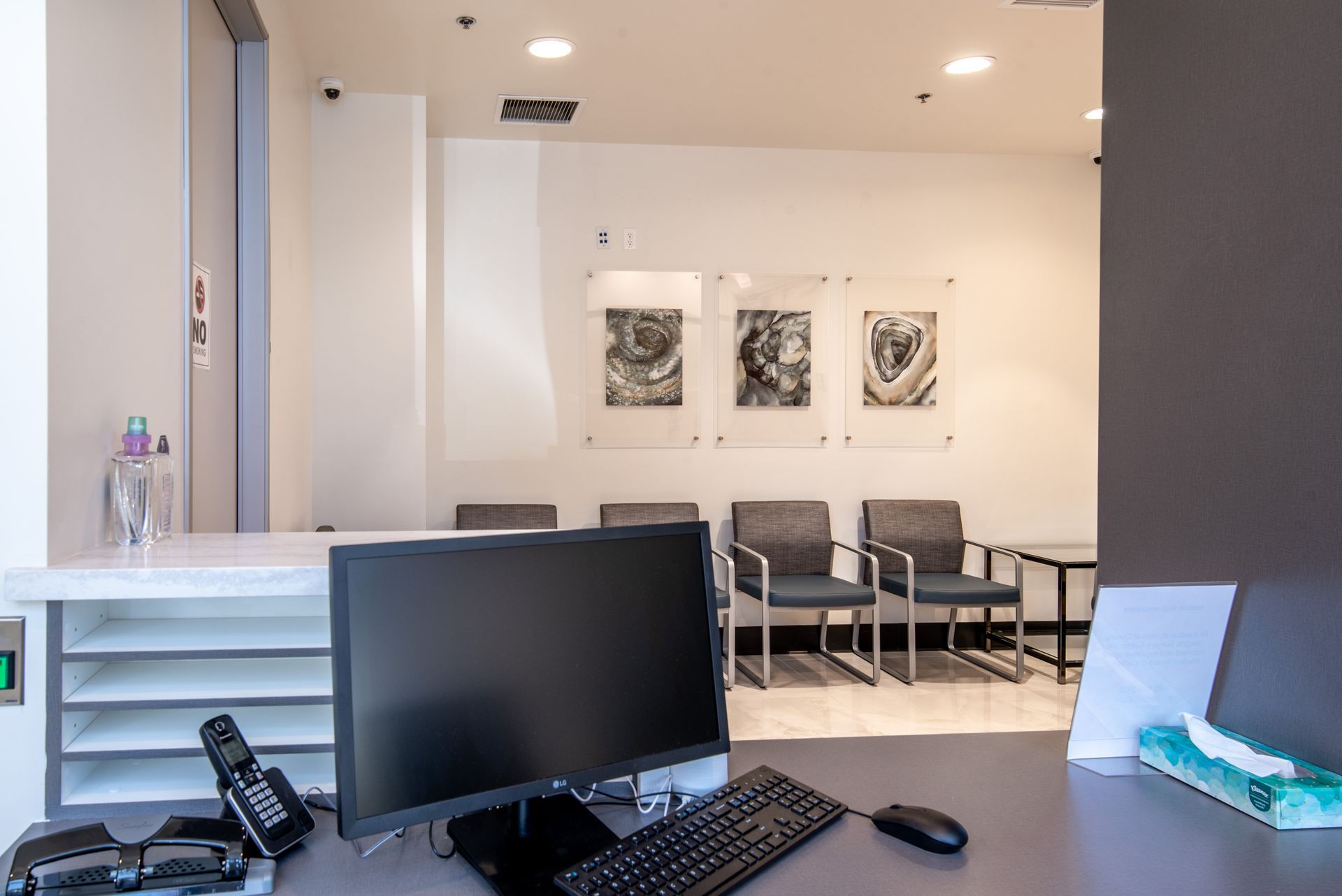 Reception area with computer, desk, chairs, and art prints.