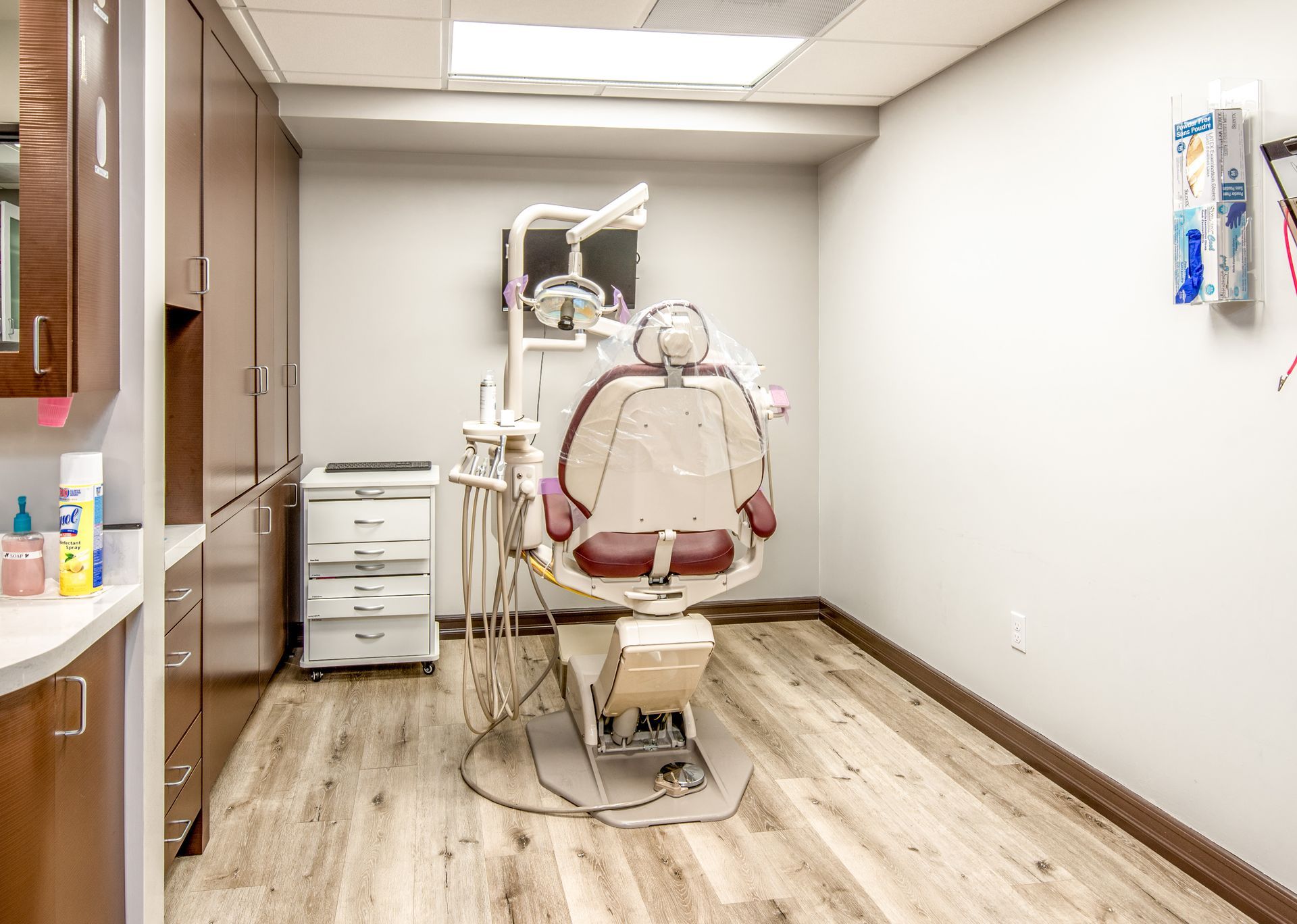 Dental office exam room with chair, tools, cabinets, and wood-look flooring.