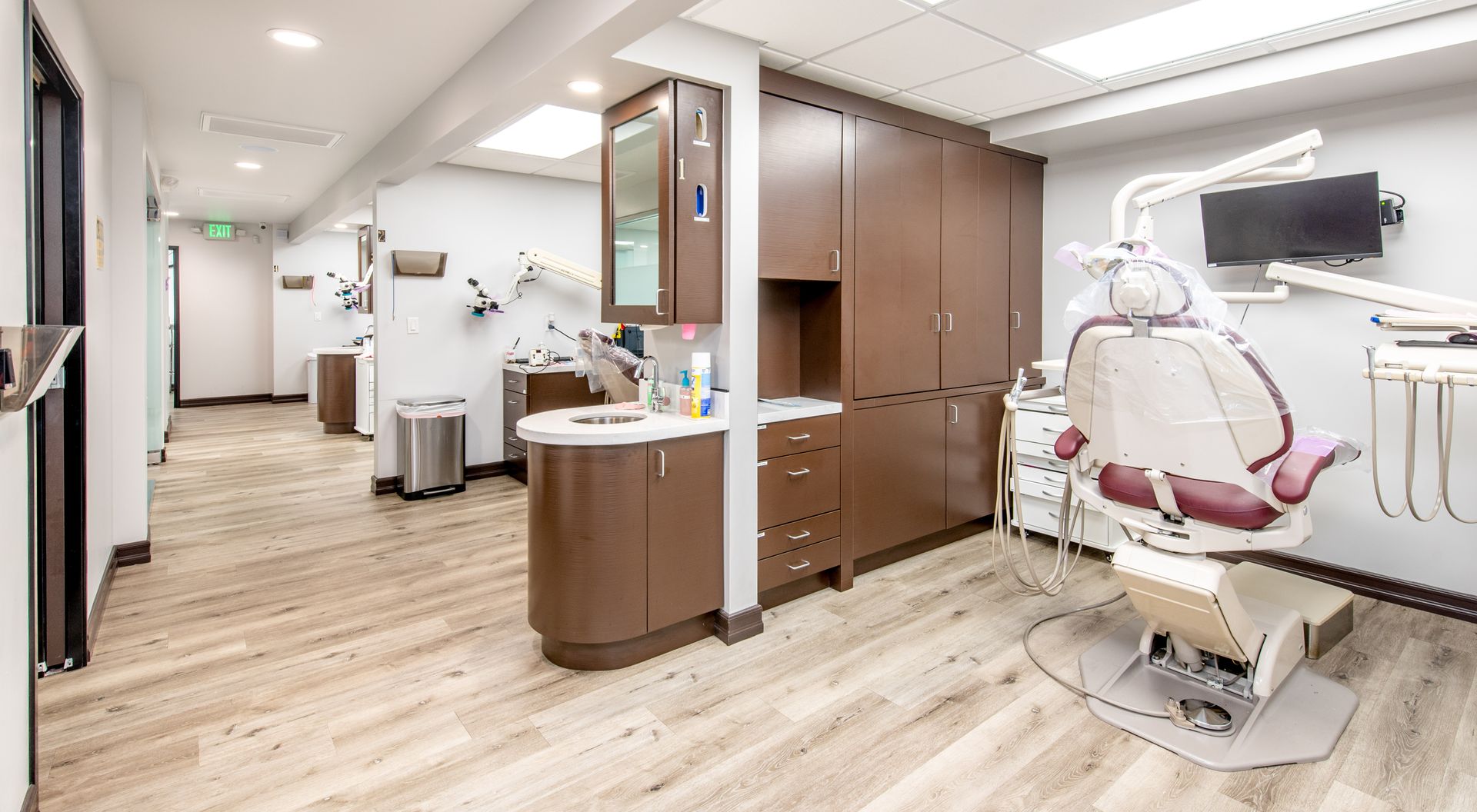 Dental office with dental chair, cabinets, and equipment. Brown and white color scheme.