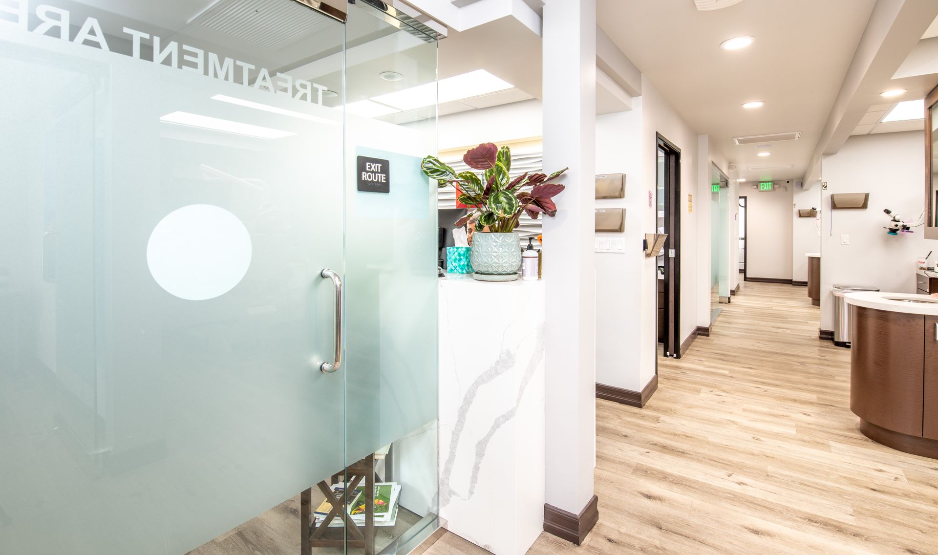 Hallway inside a dental office with treatment rooms and a frosted glass door. Wooden floors.