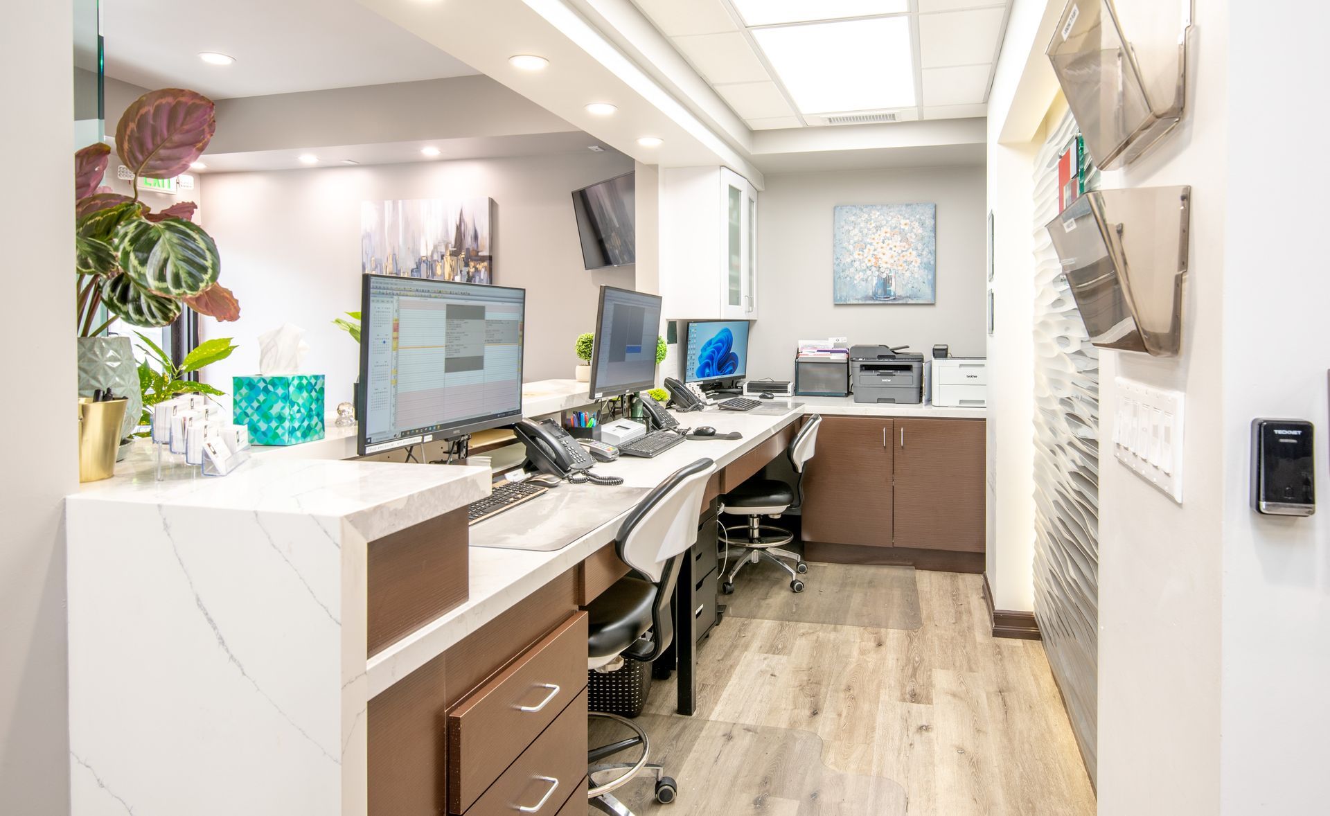 Reception desk in a modern office. Counter with computers, a printer, and decor. Wooden floor.